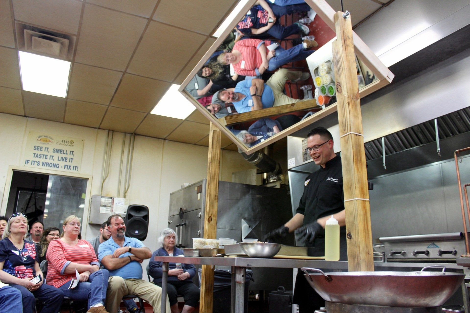 A man is cooking in front of a group of people in a kitchen.