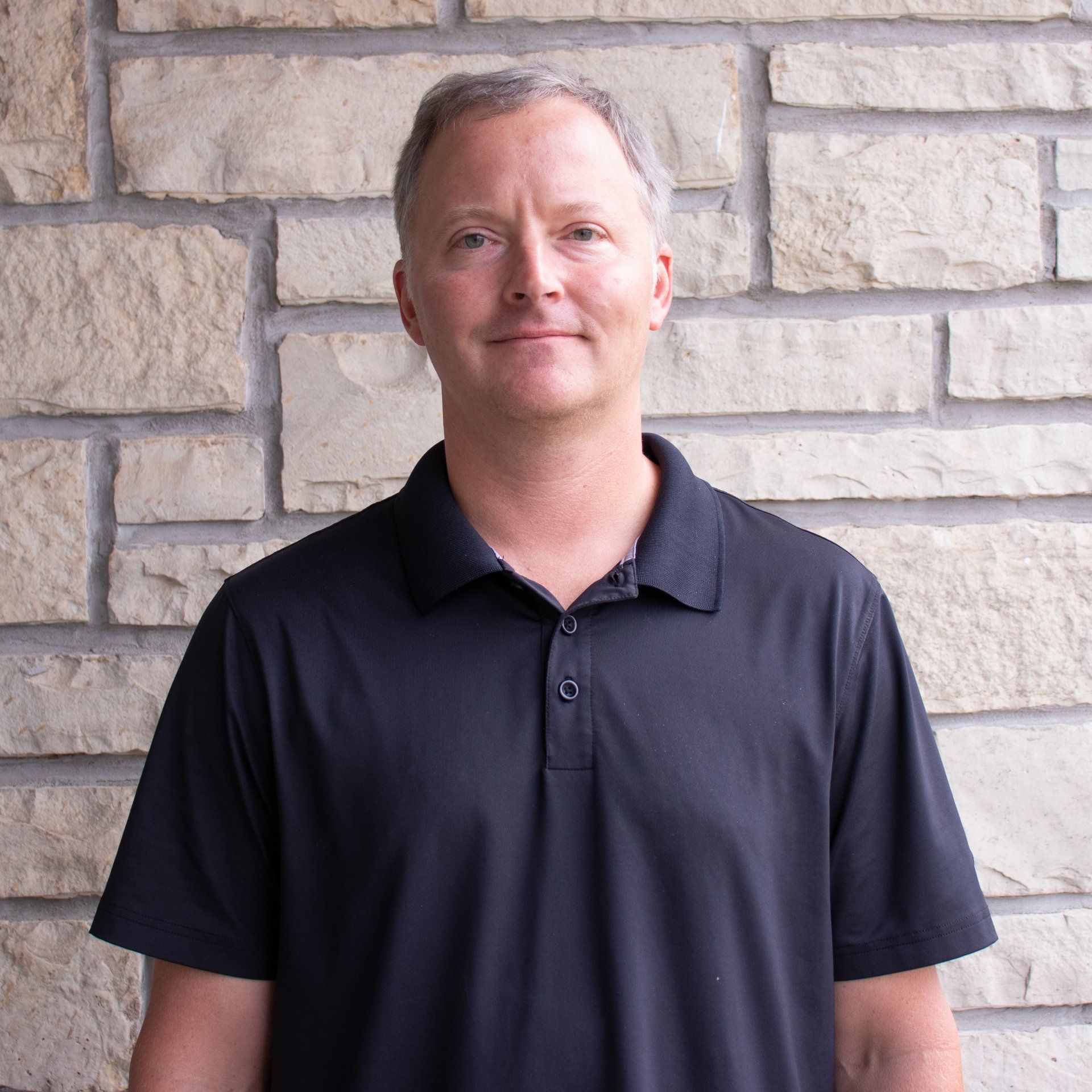 A man in a black shirt is standing in front of a brick wall