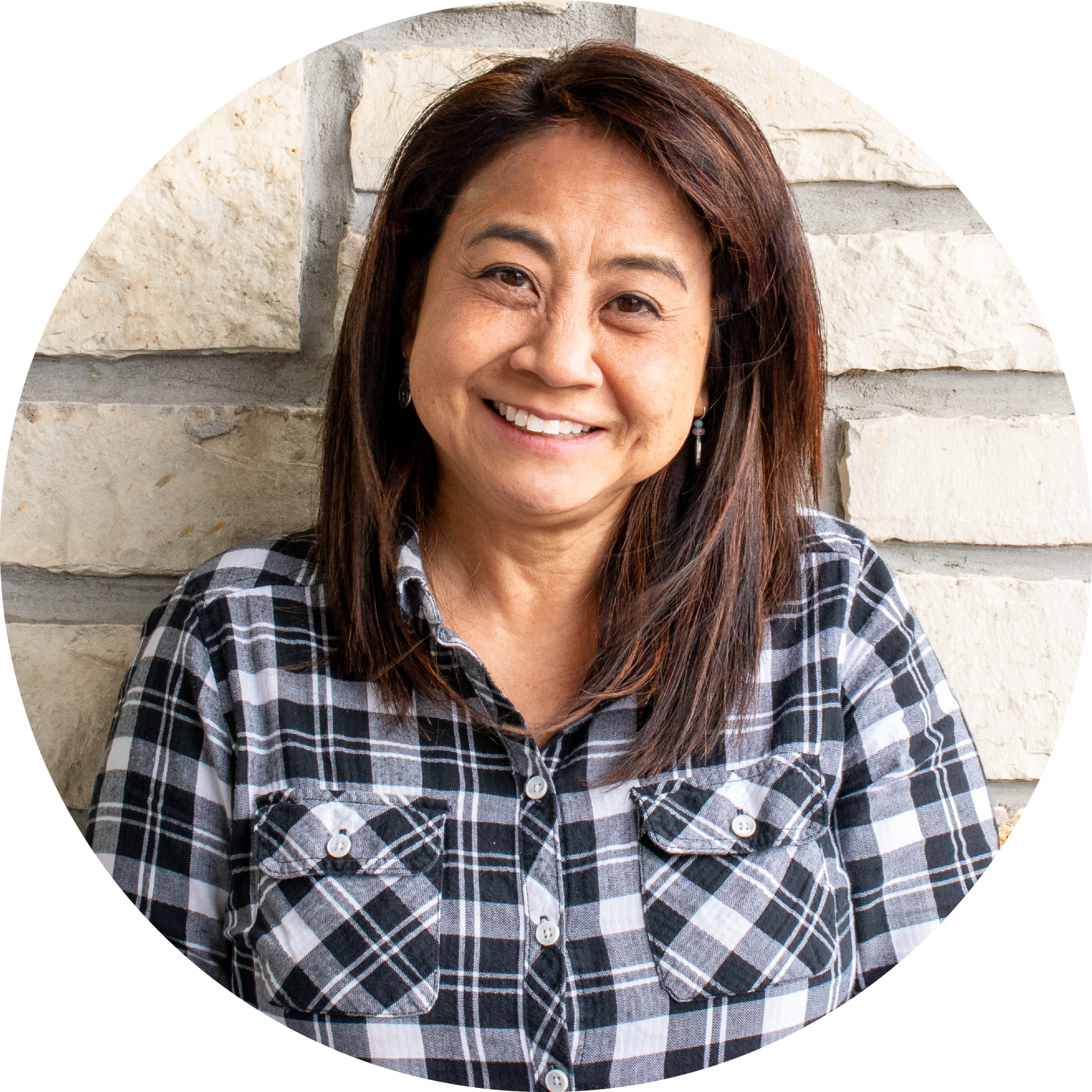 A woman in a plaid shirt is smiling in front of a brick wall.