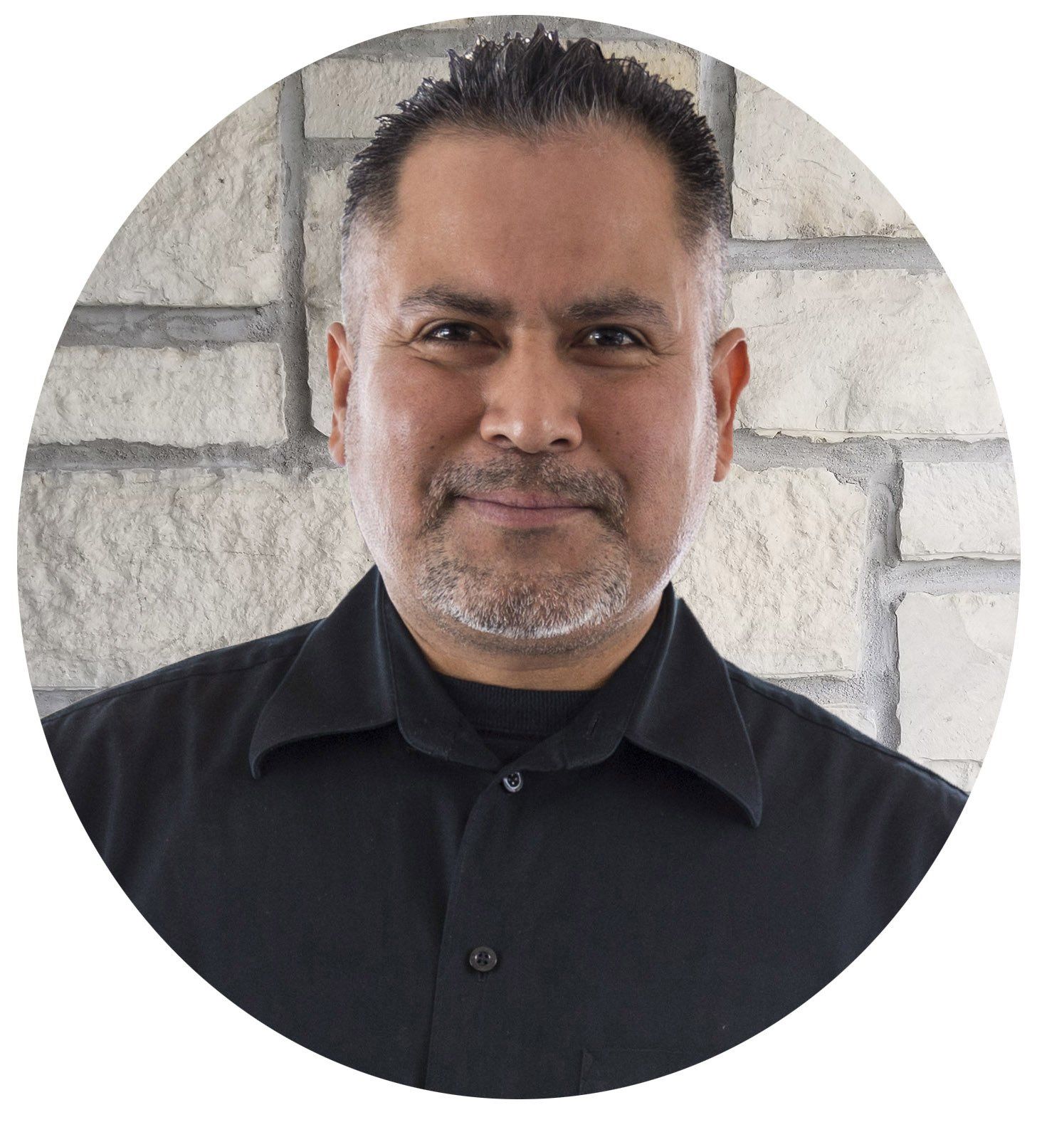 A man in a black shirt is standing in front of a brick wall.