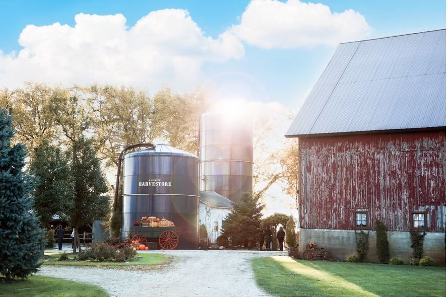 A large red barn and black silo in the woods. 
