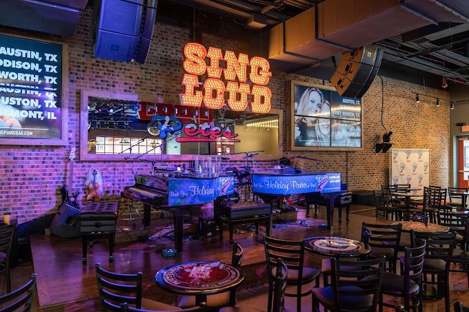 A restaurant with tables and chairs and a stage with a sign that says sing loud.