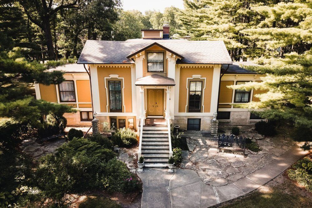 A yellow house with steps leading to the front door sits in a forest.