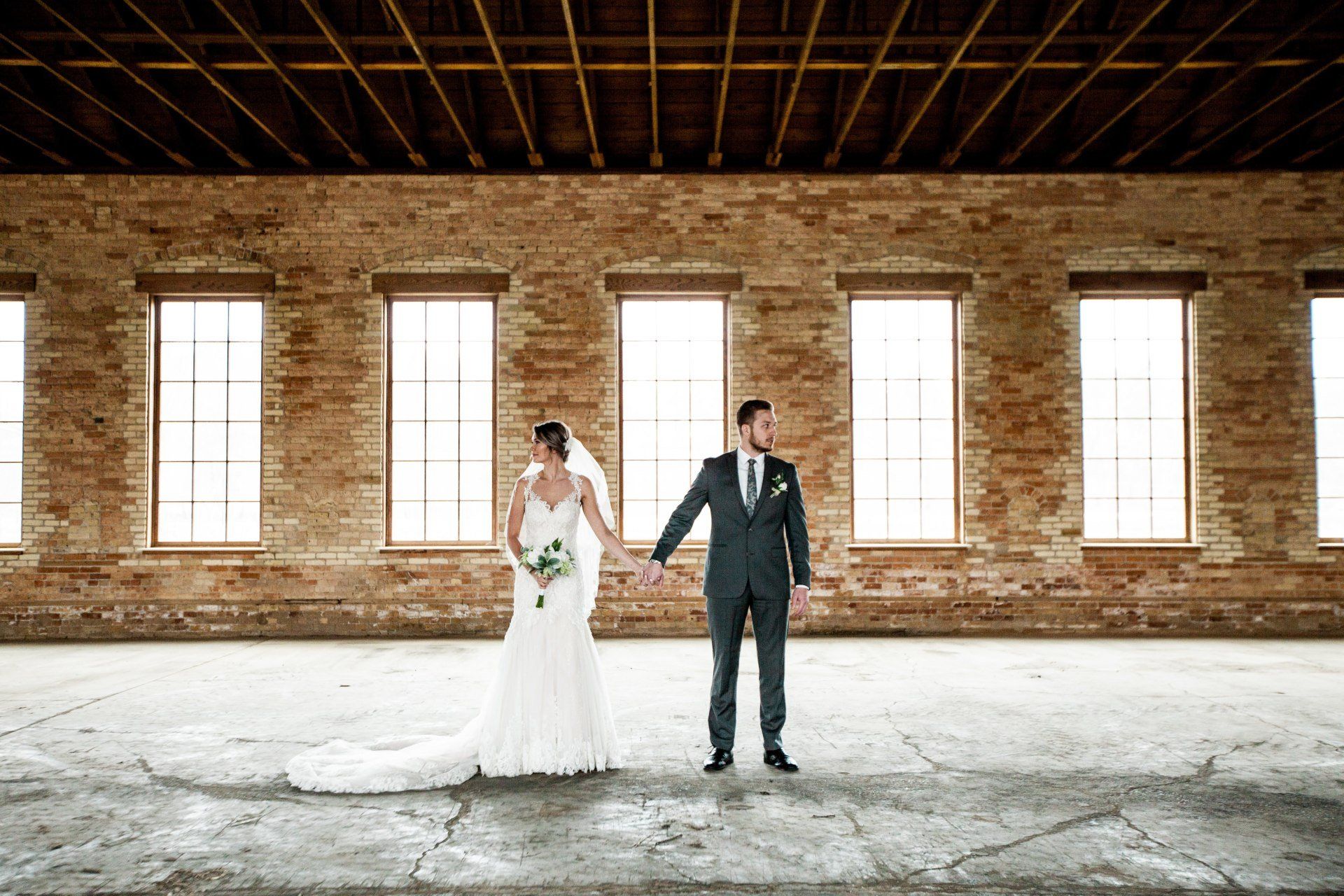 A bride and groom are holding hands in front of a brick wall.