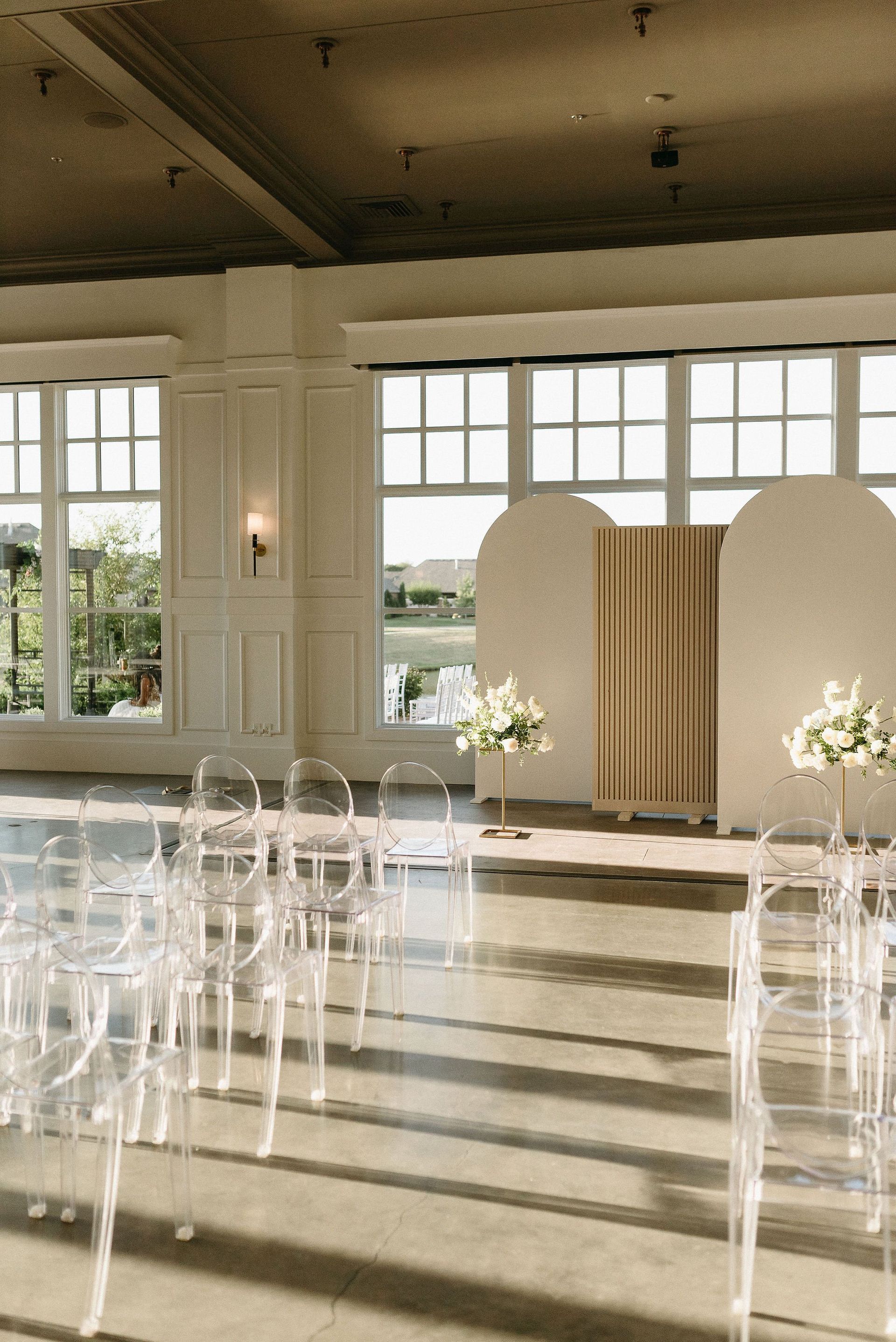 A room with a row of clear chairs and flowers on the floor.