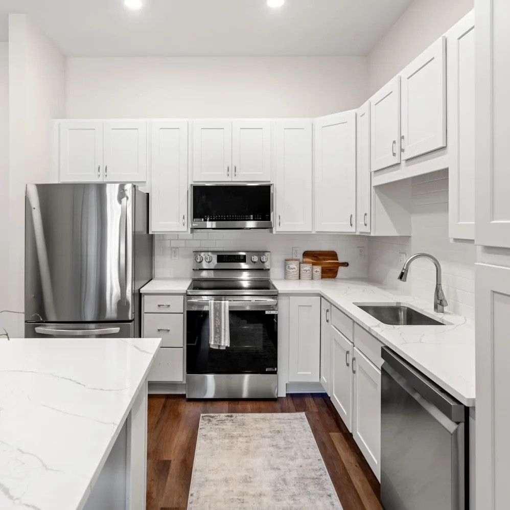 White kitchen with stainless steel appliances, white cabinets, and a marble countertop.