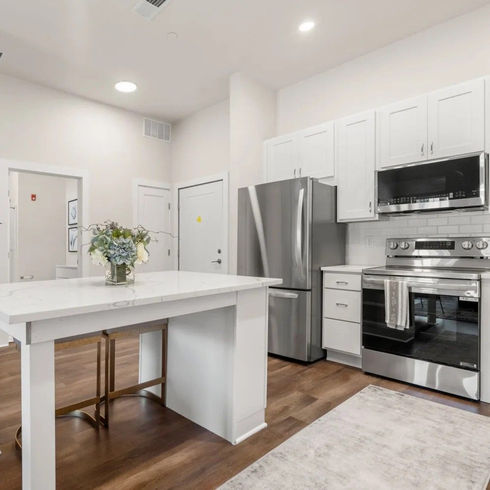Modern kitchen with white cabinets, stainless steel appliances, and a marble countertop island.