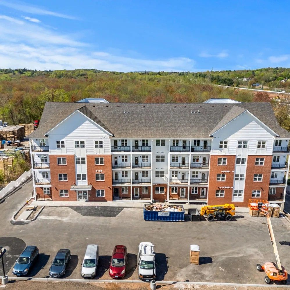 Exterior of a new multi-story apartment building with red brick and white siding. Cars parked in front.