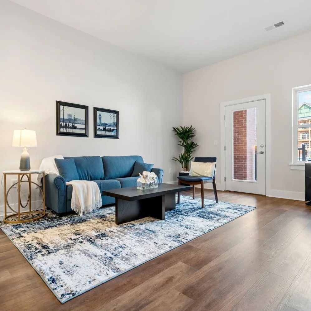 Living room with blue sofa, black coffee table, and patterned rug. Door to exterior visible.