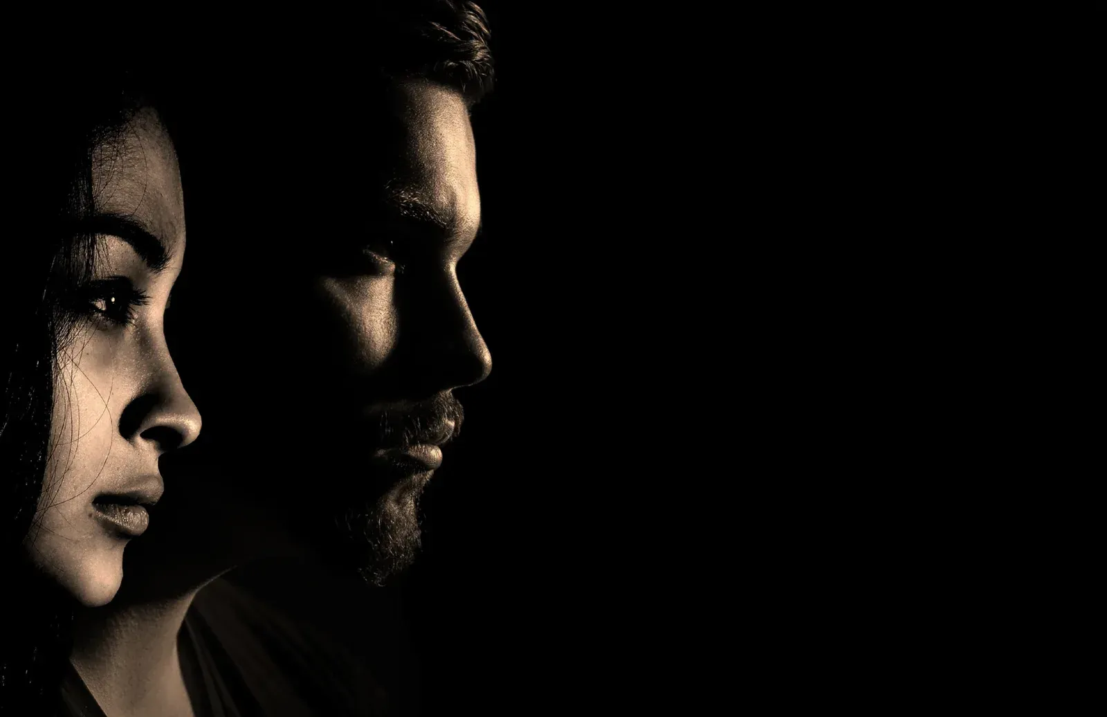 Woman and man in profile, faces in partial shadow against a black background.