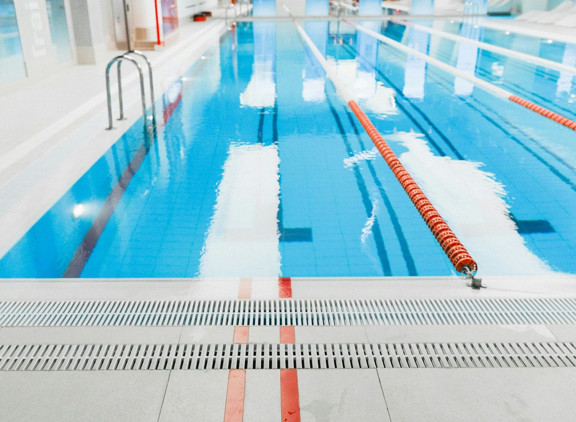 A handyman wearing work gloves carefully lays ceramic tiles in the bottom of a swimming pool, carefully aligning each piece.