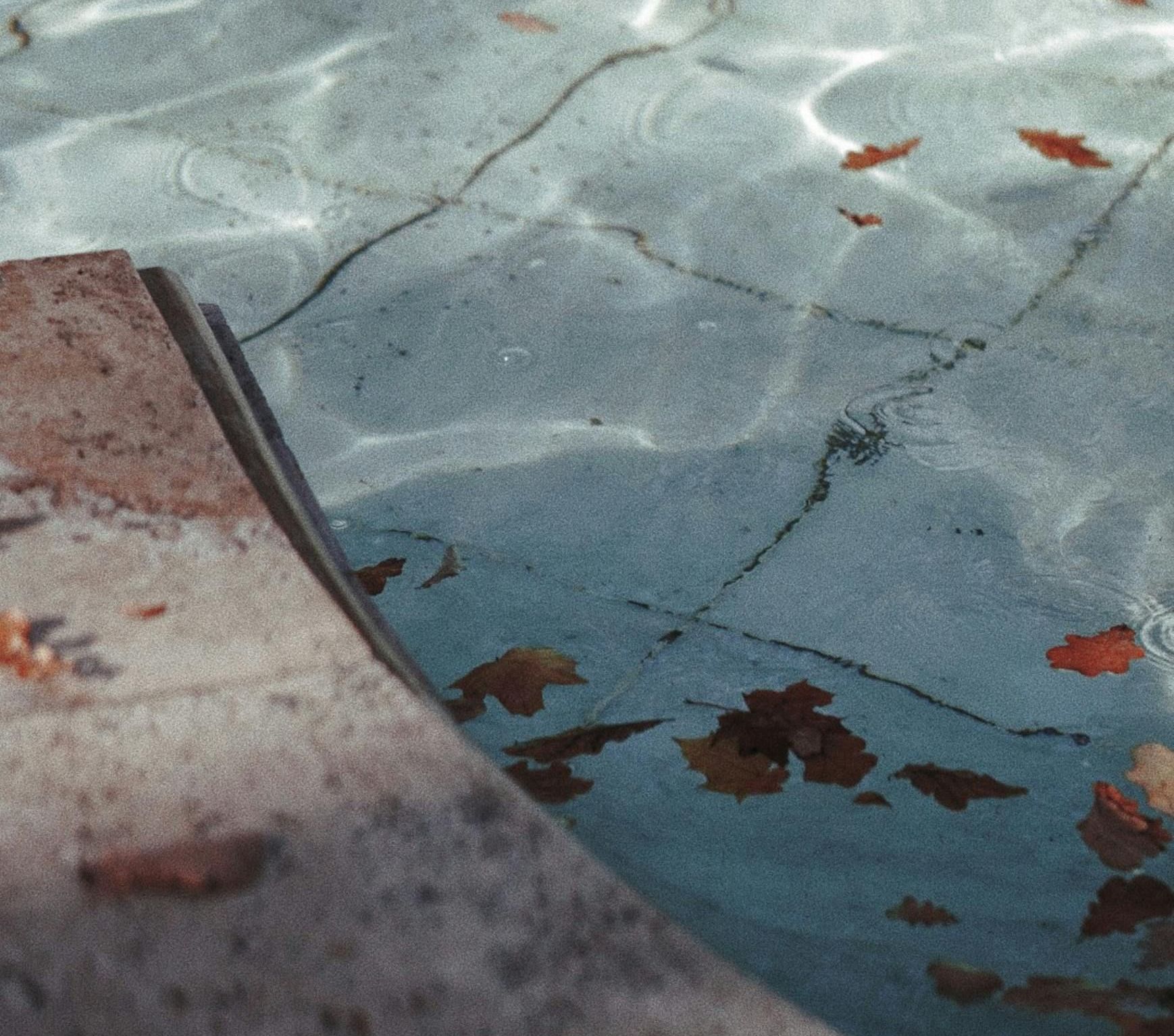 A handyman wearing work gloves carefully lays ceramic tiles in the bottom of a swimming pool, carefully aligning each piece.