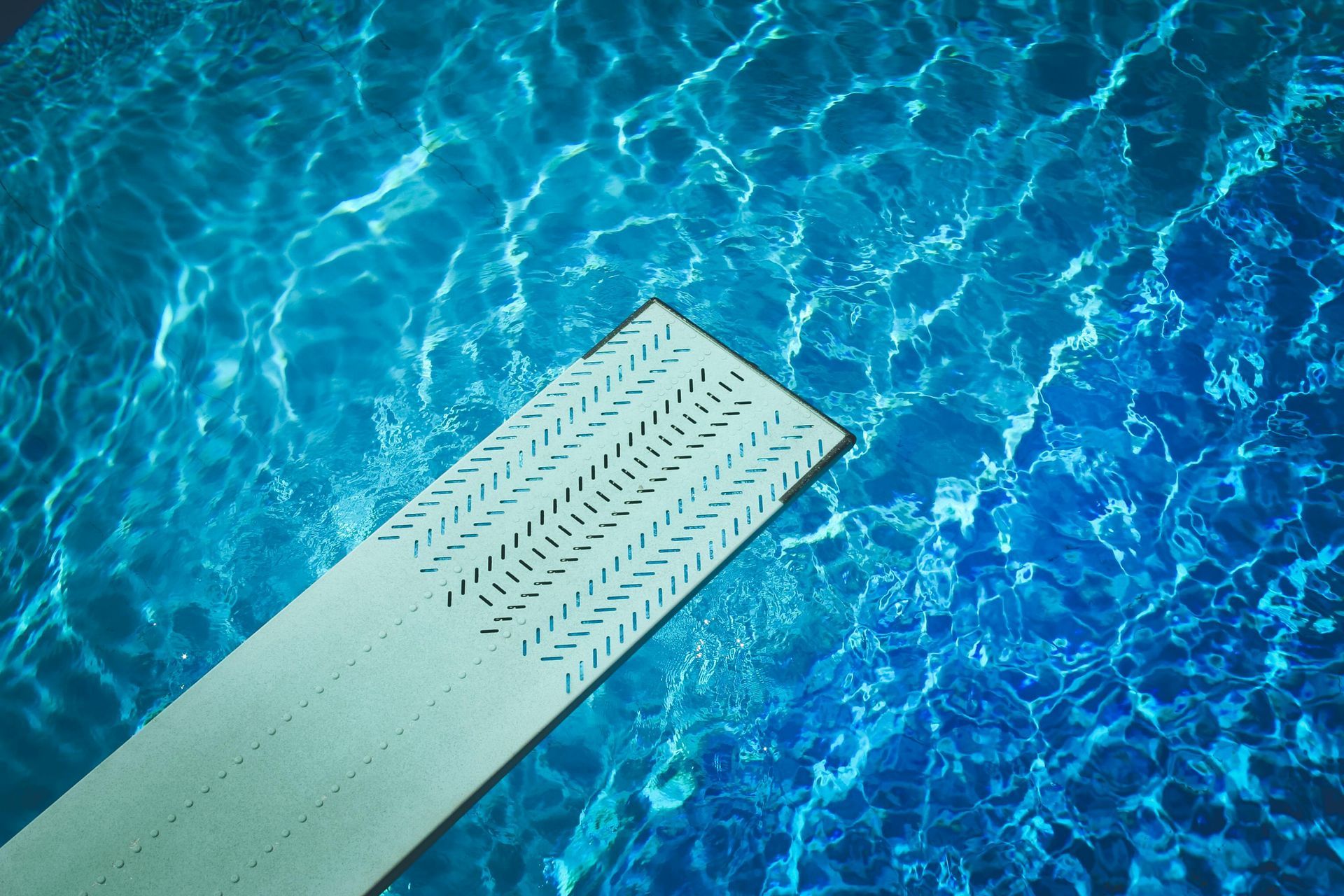 A handyman wearing work gloves carefully lays ceramic tiles in the bottom of a swimming pool, carefully aligning each piece.