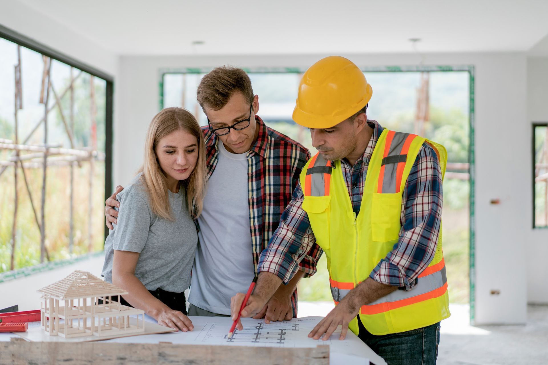Worker shows blueprints to couple inside construction house, highlighting home remodeling service.