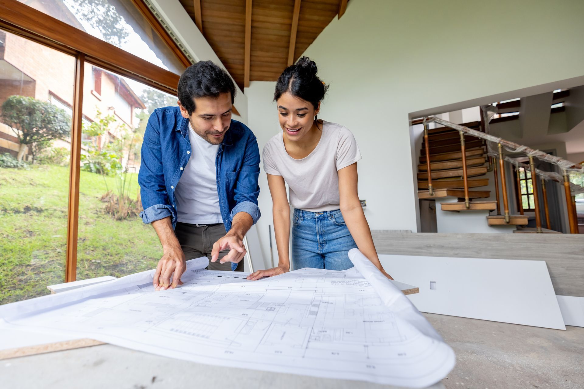 A happy couple is looking at the blueprints for their residential remodeling project. A man uses an electric drill to install siding during a home remodeling project outdoors.