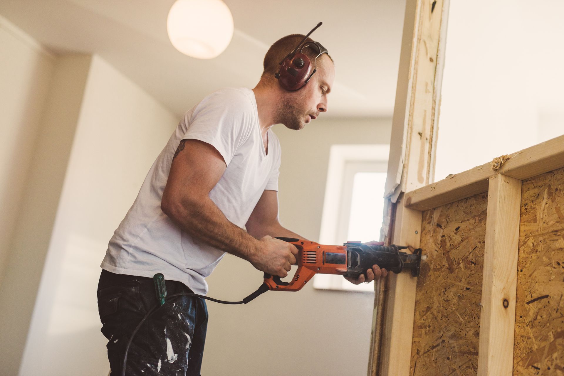 A man uses an electric drill to install siding during a home remodeling project outdoors. A man uses an electric drill to install siding during a home remodeling project outdoors.