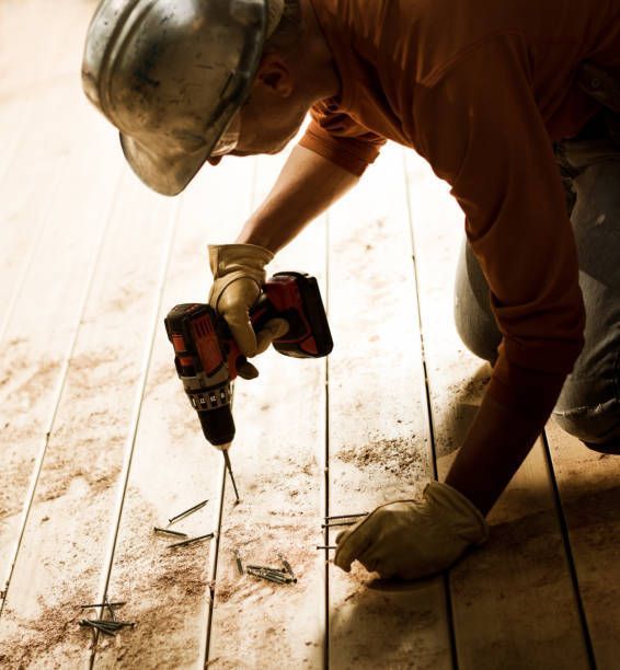 Construction worker fastening wood deck with battery-powered drill.