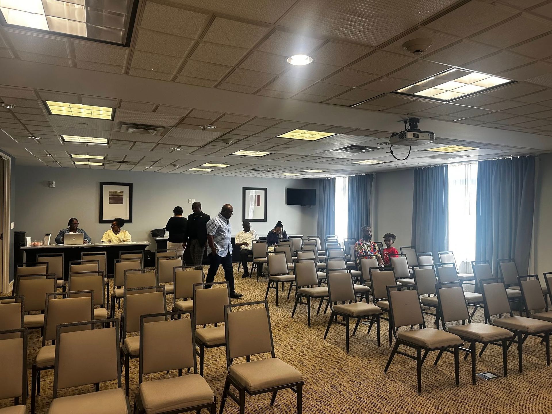 A large room filled with chairs and people standing around a table.