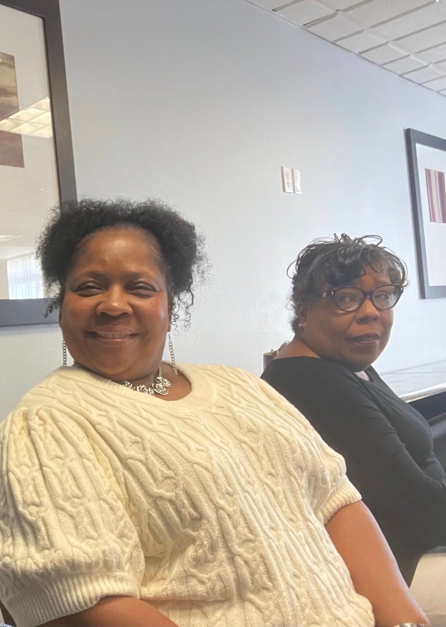 Two women are sitting next to each other in a room and smiling.