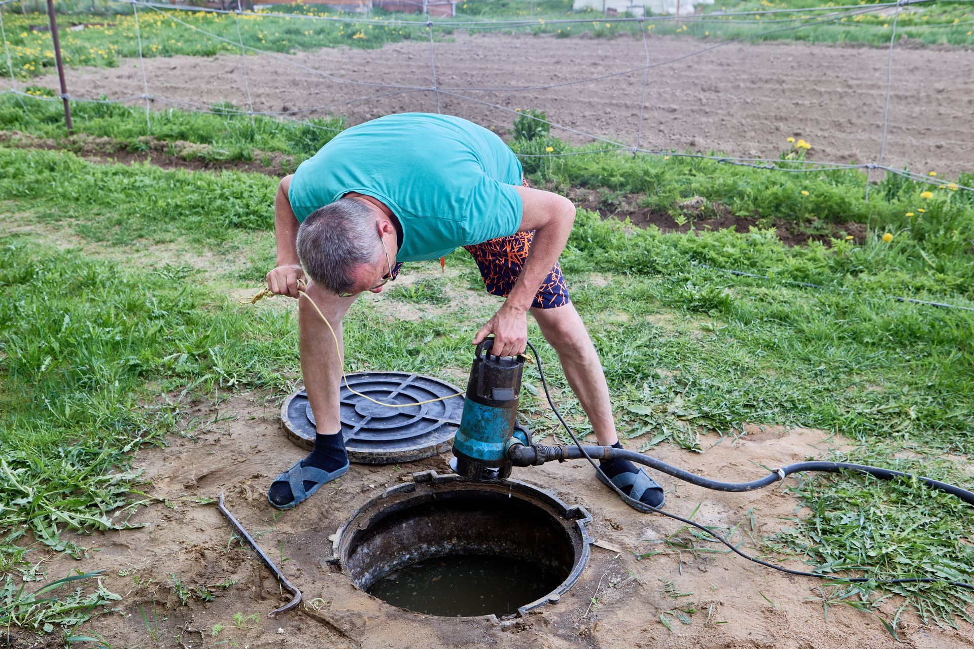 Man operating a pump from an open well, outdoors.