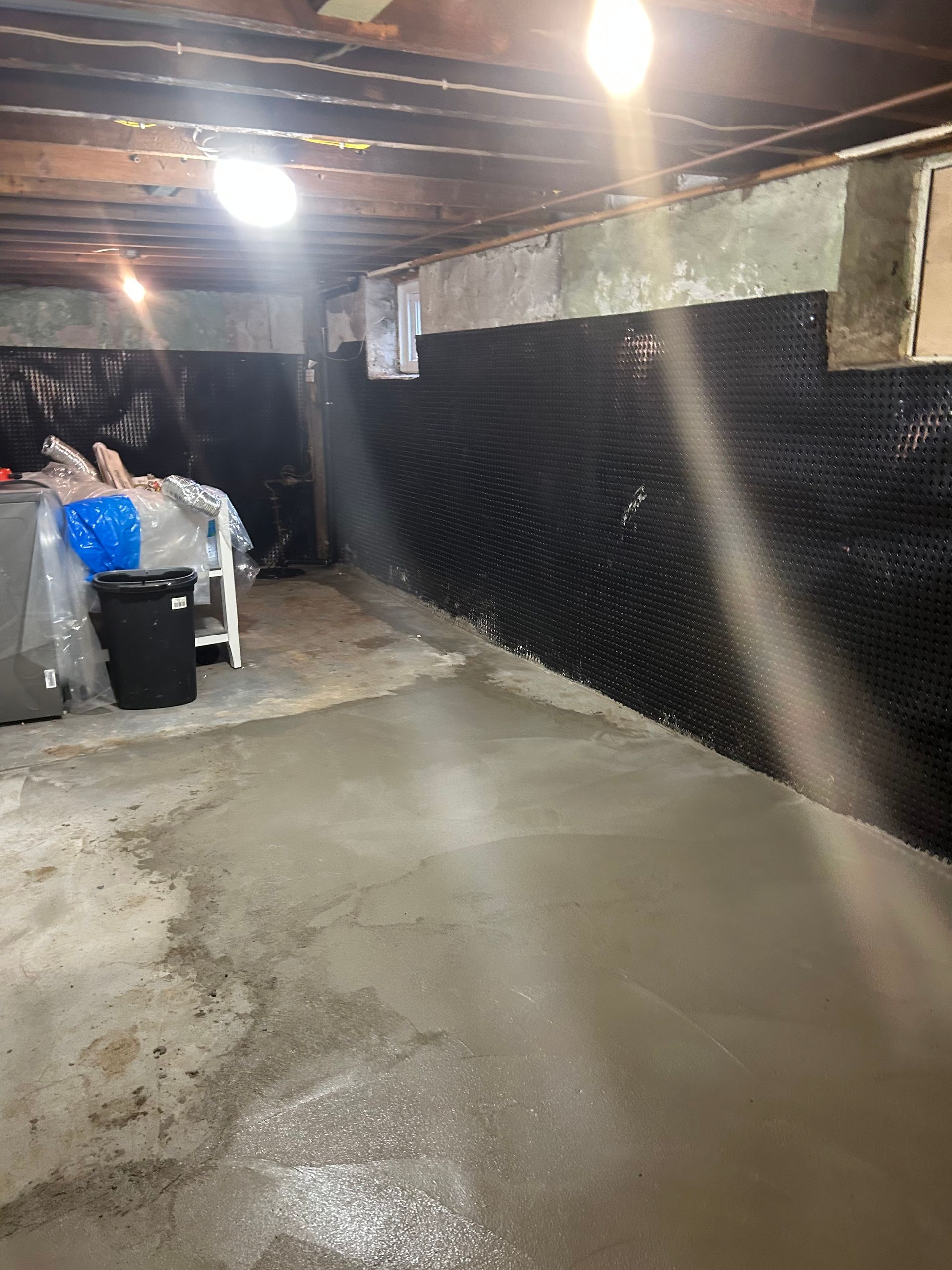 Basement with newly poured concrete floor and black dimpled wall membrane.