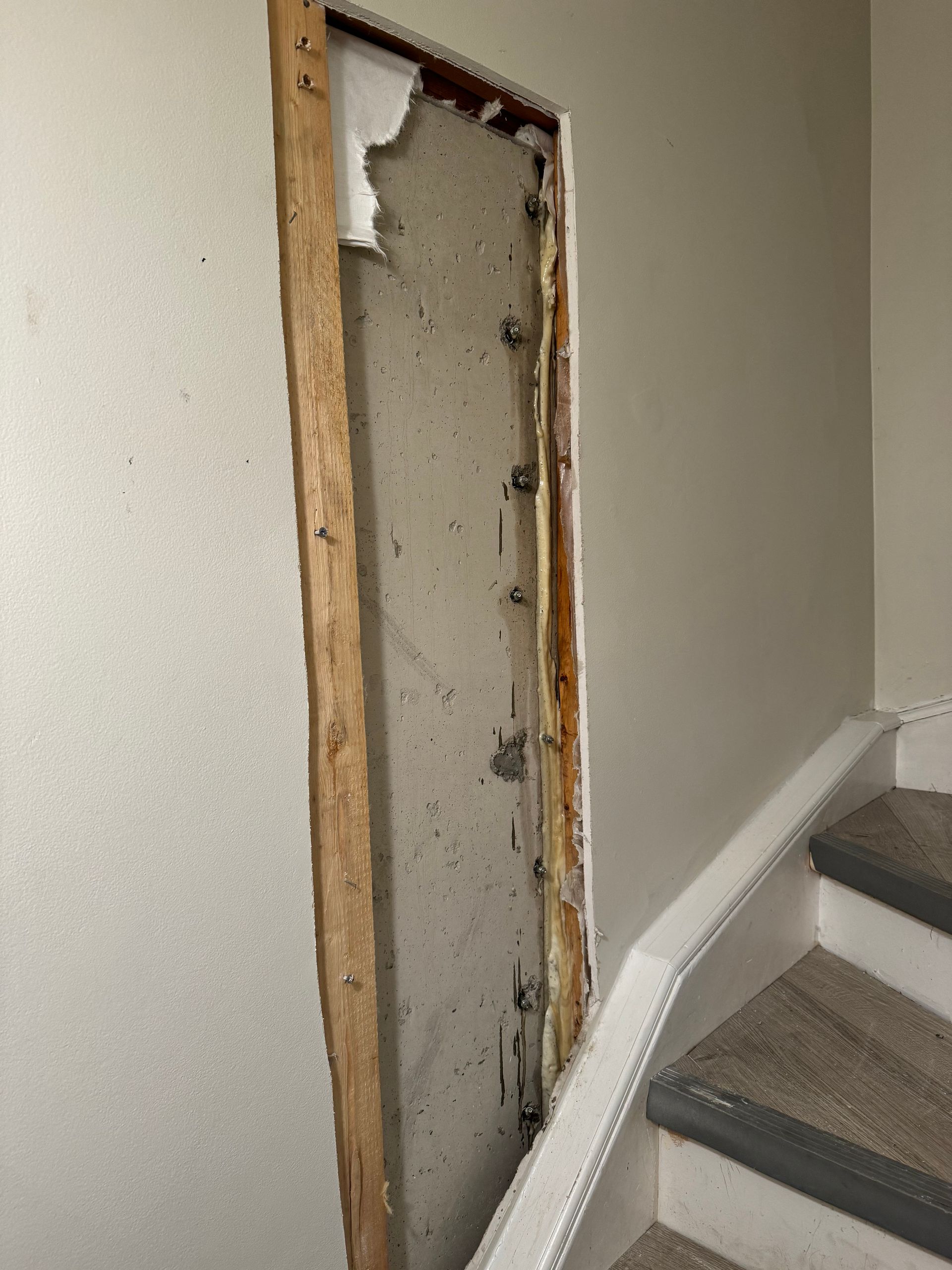 Damaged wall opening with exposed wood frame next to a staircase.