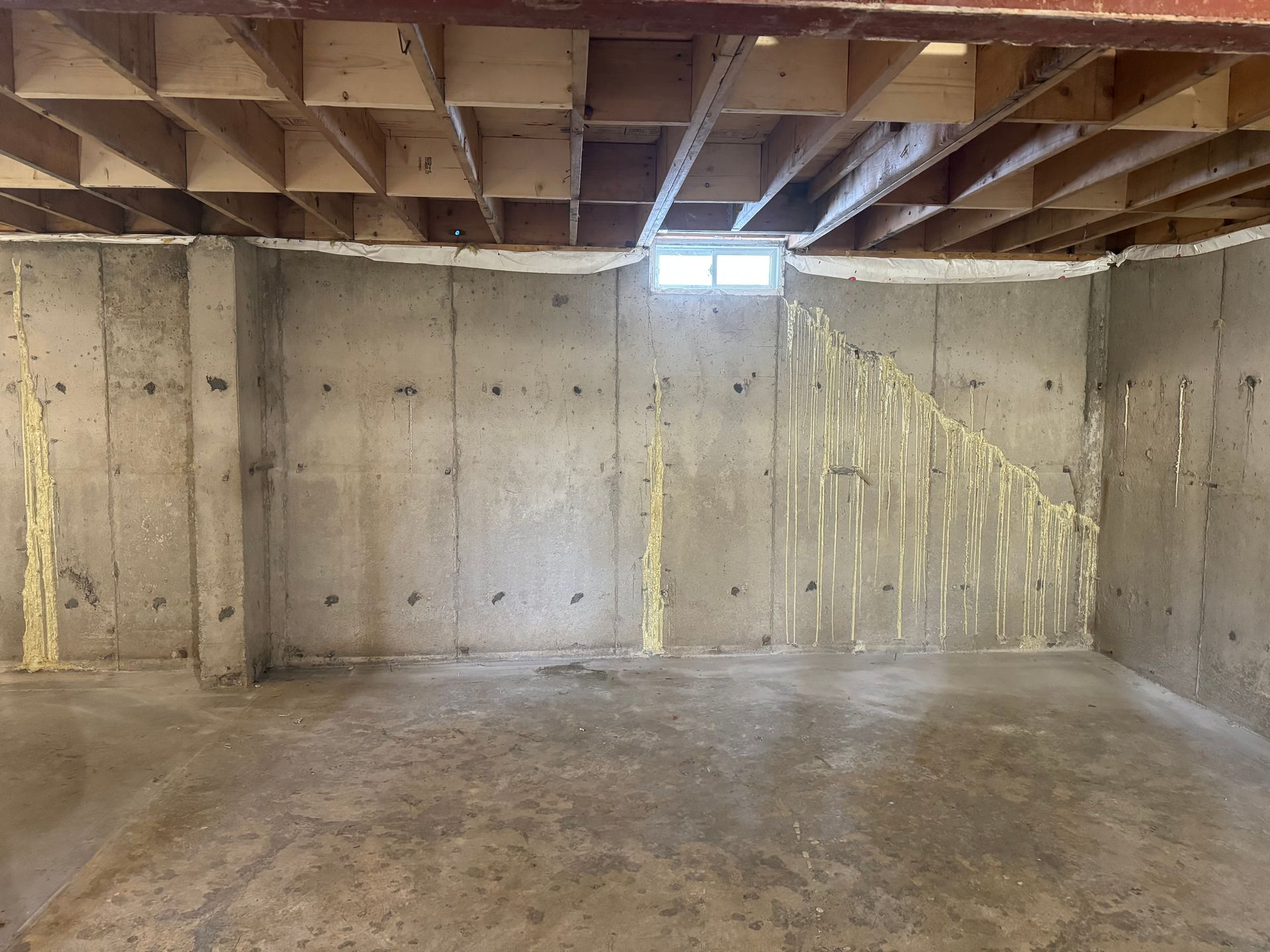 Basement with concrete walls and floor. Insulation foam is visible. Overhead, there's a wood ceiling.