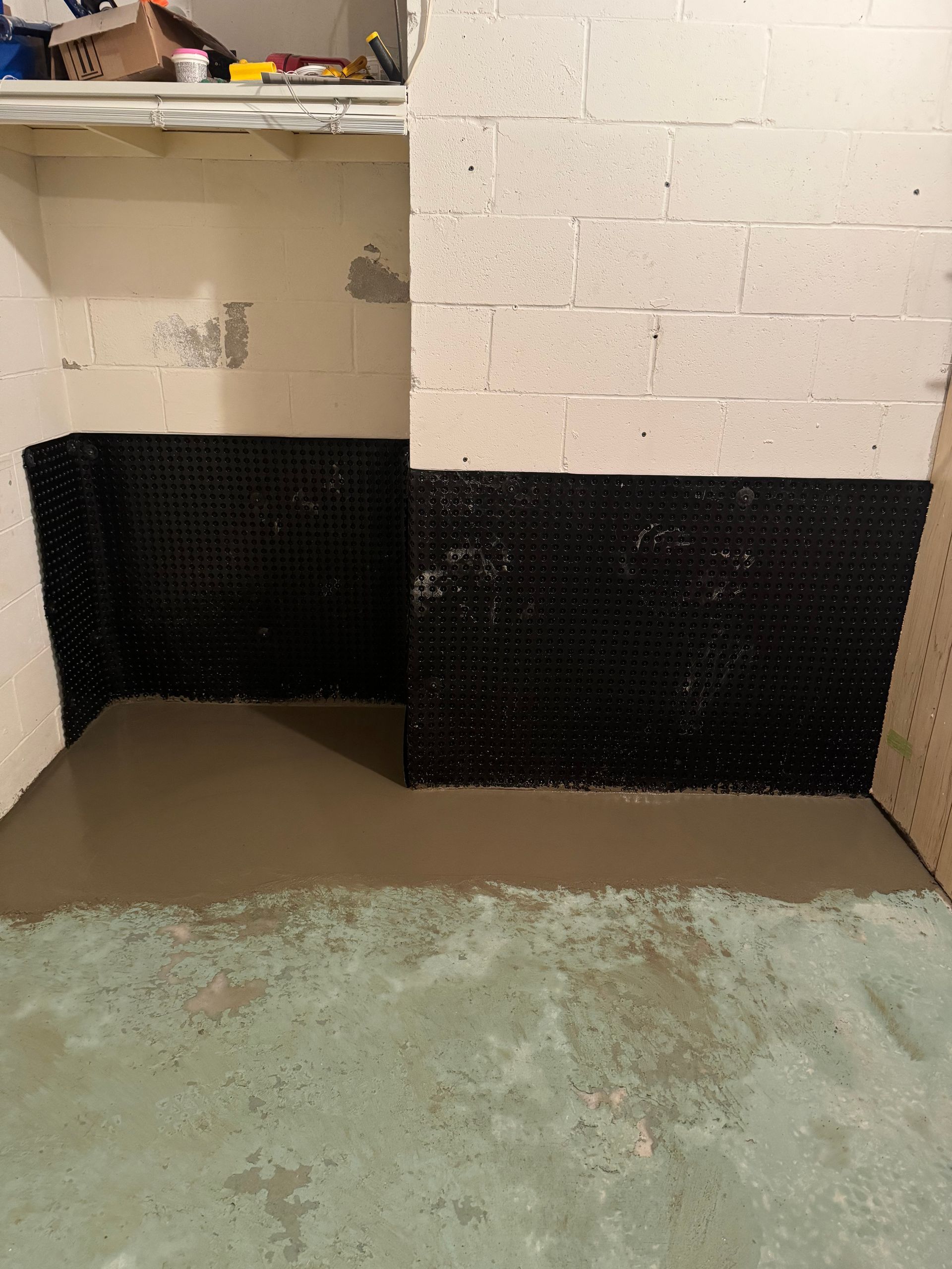 Basement with black waterproofing membrane on walls, new concrete floor, and white cinder block walls.