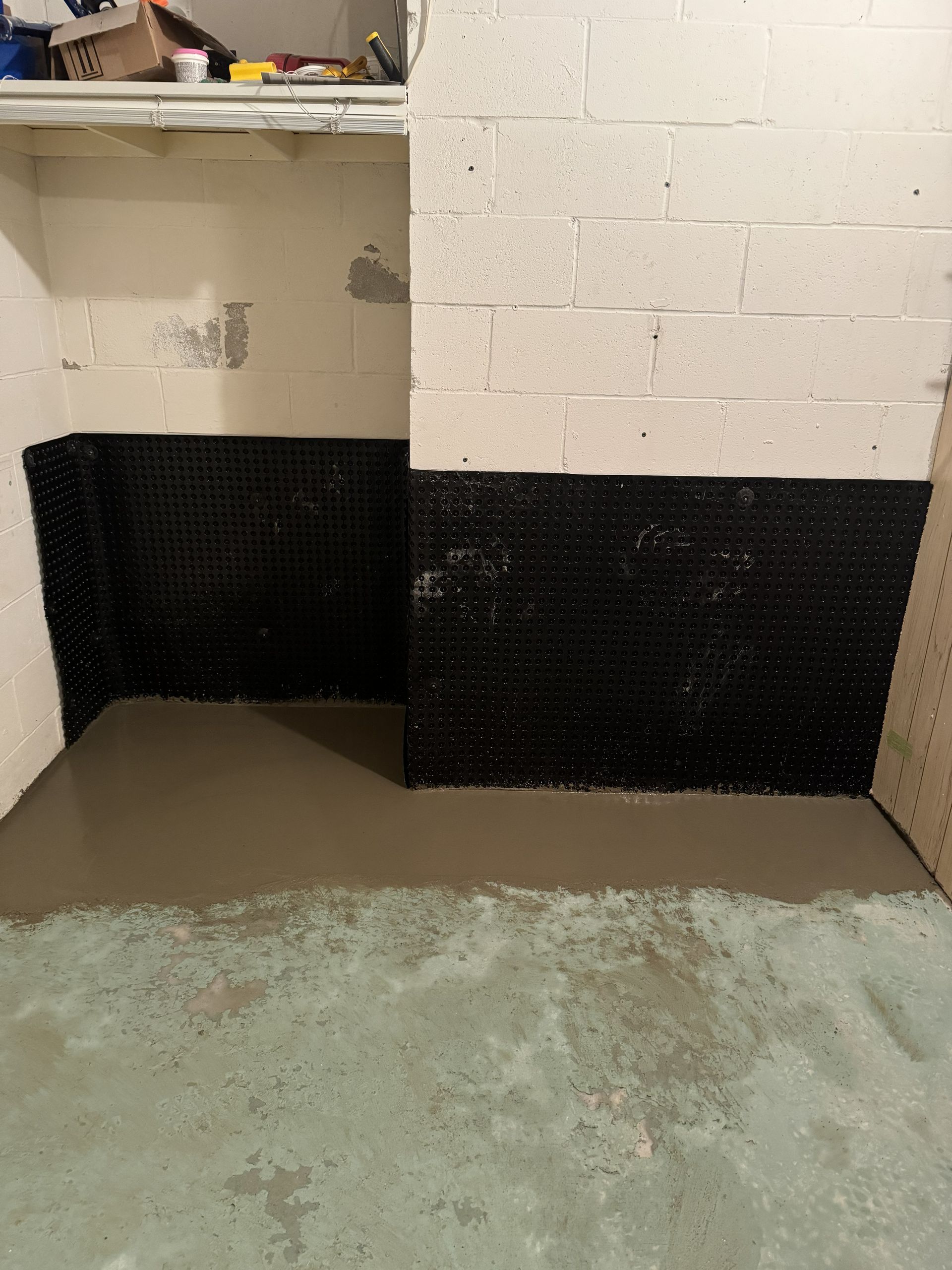 Basement with newly poured concrete floor, black wall barrier, and white block walls.