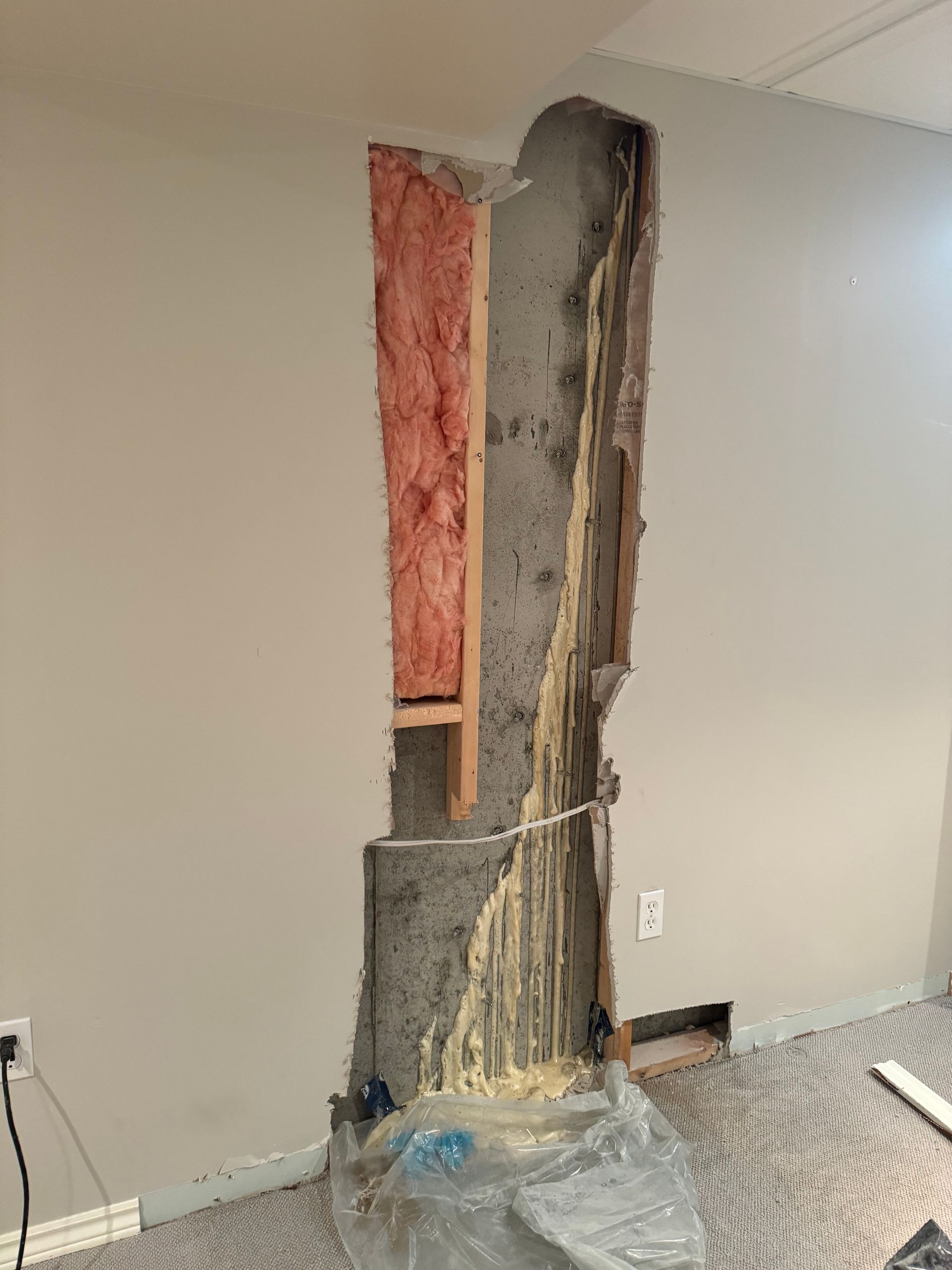 A section of wall cut open, revealing insulation and a cement structure, with a power outlet visible.