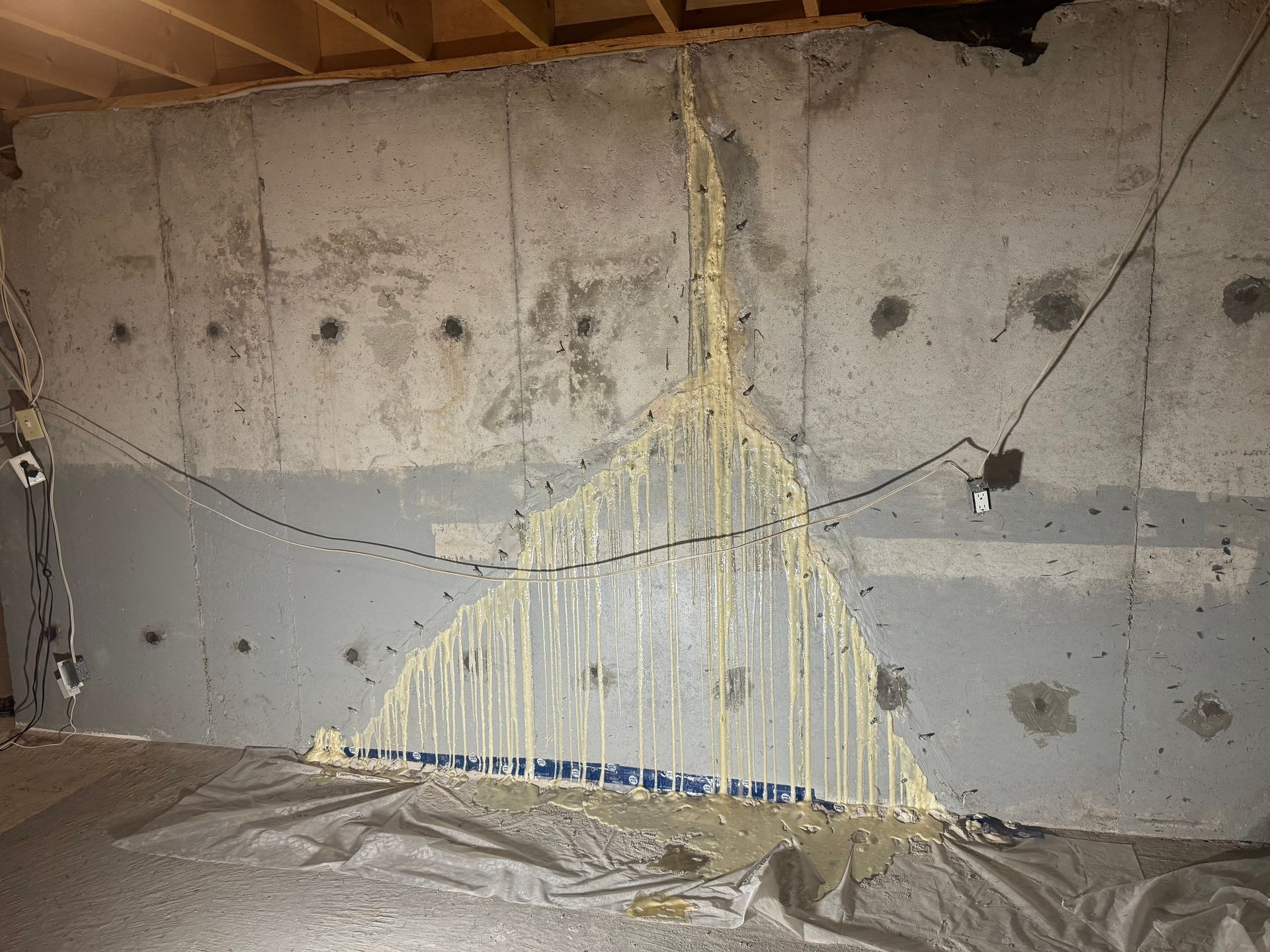 Concrete basement wall with a large crack filled with yellow sealant, drips.