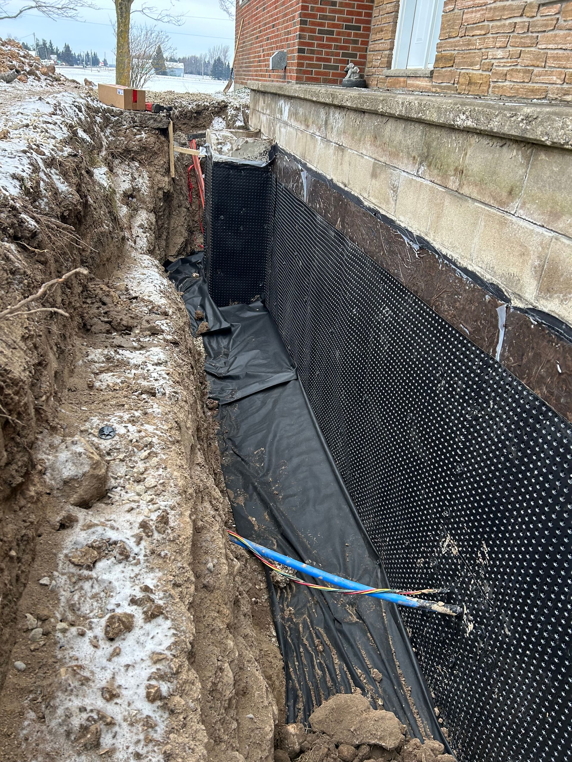 A foundation being excavated, revealing a black drainage membrane against the concrete wall.