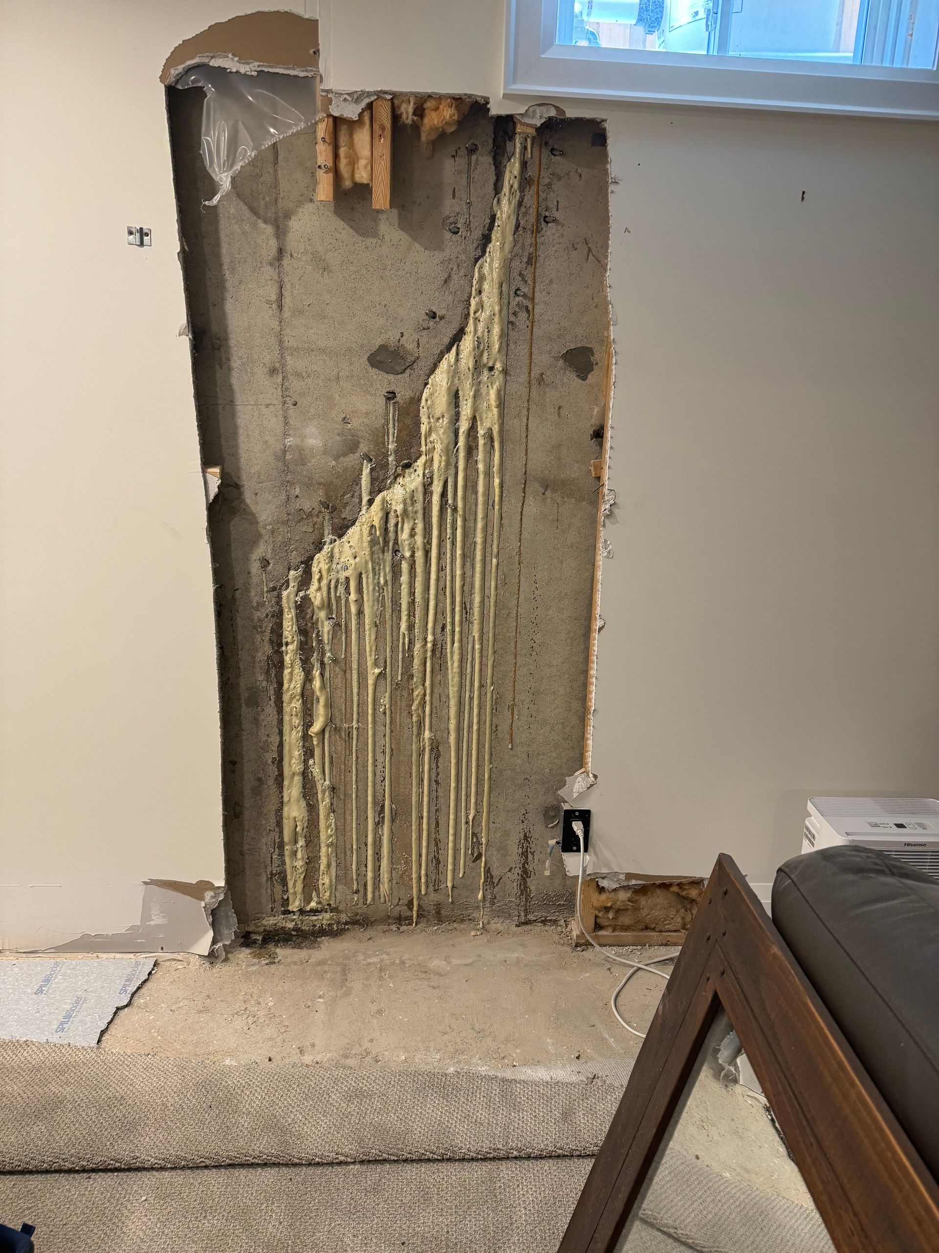 Exposed concrete and wood framing within a wall opening, with yellow expanding foam visible.