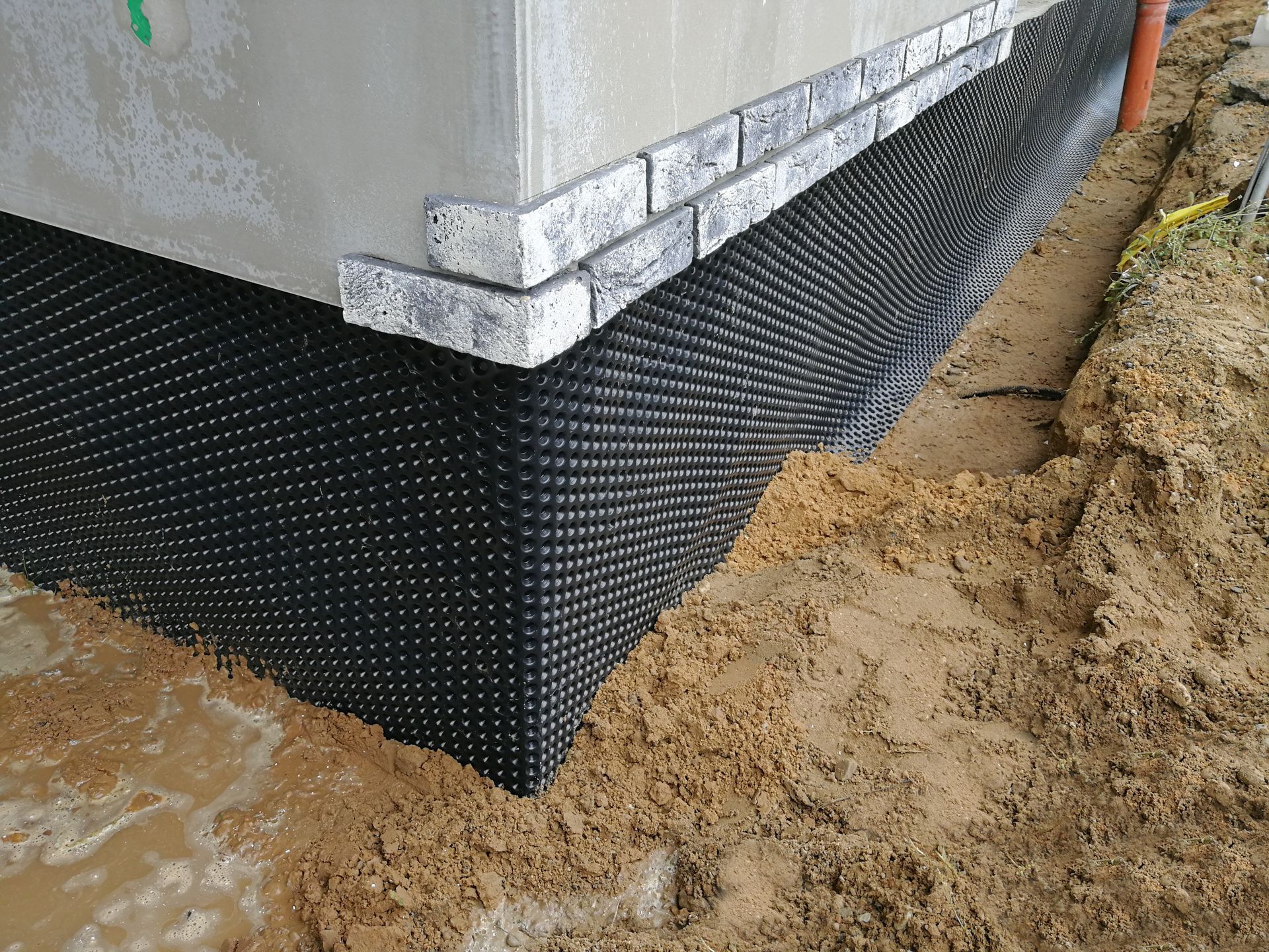 Foundation of a building with black dimpled drainage membrane and brick veneer.