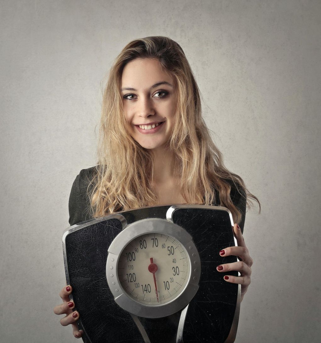 Woman holding a scale, smiling, against a neutral backdrop.