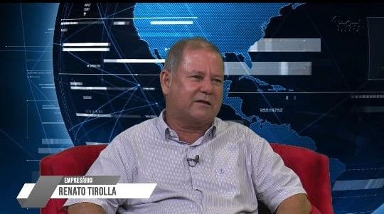 Um homem está sentado em uma cadeira com um crachá que diz Renato Tirolla