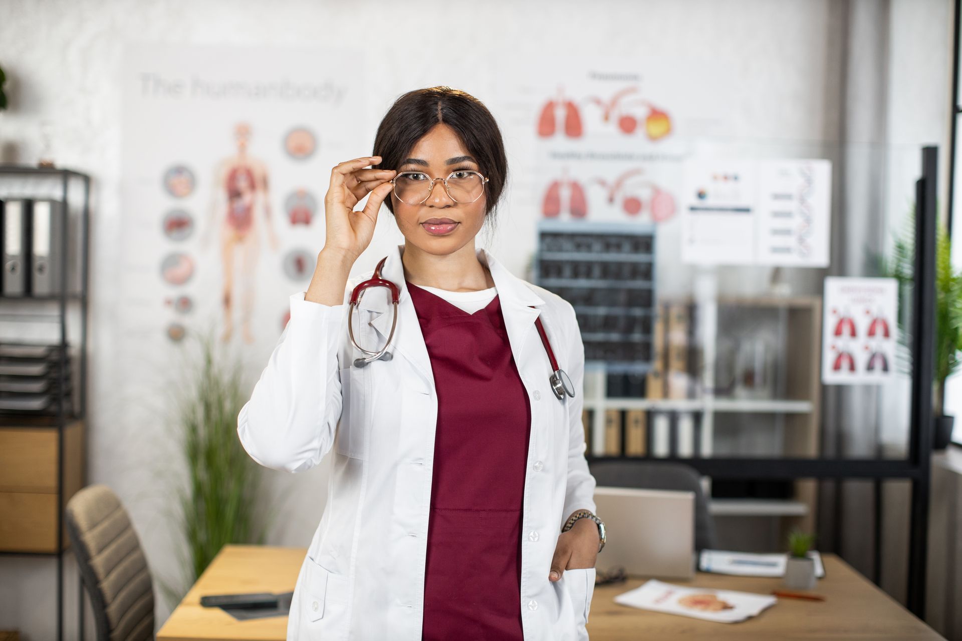 A female doctor wearing glasses and a lab coat is standing in an office.