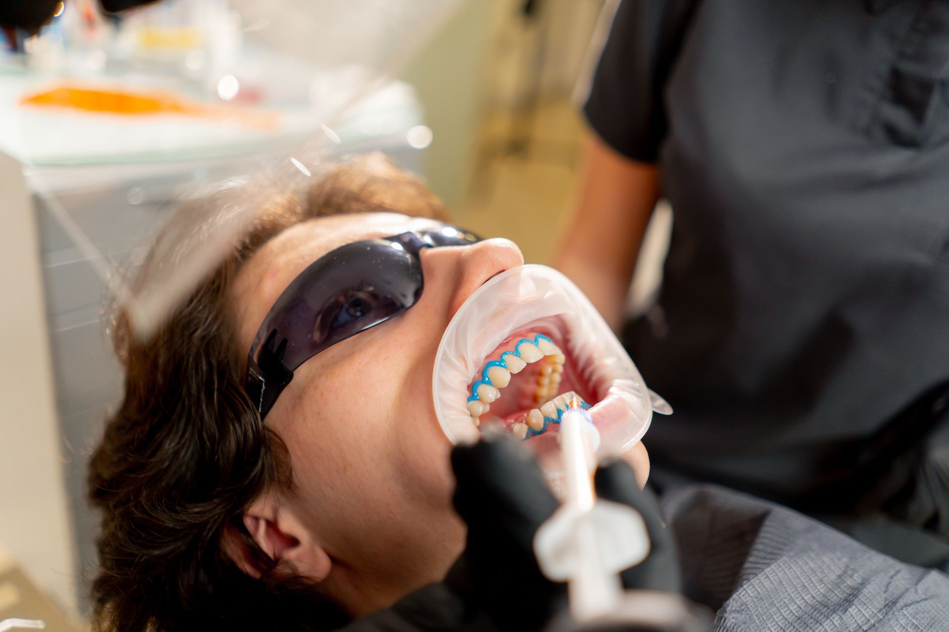 A woman is getting her teeth whitened by a dentist.