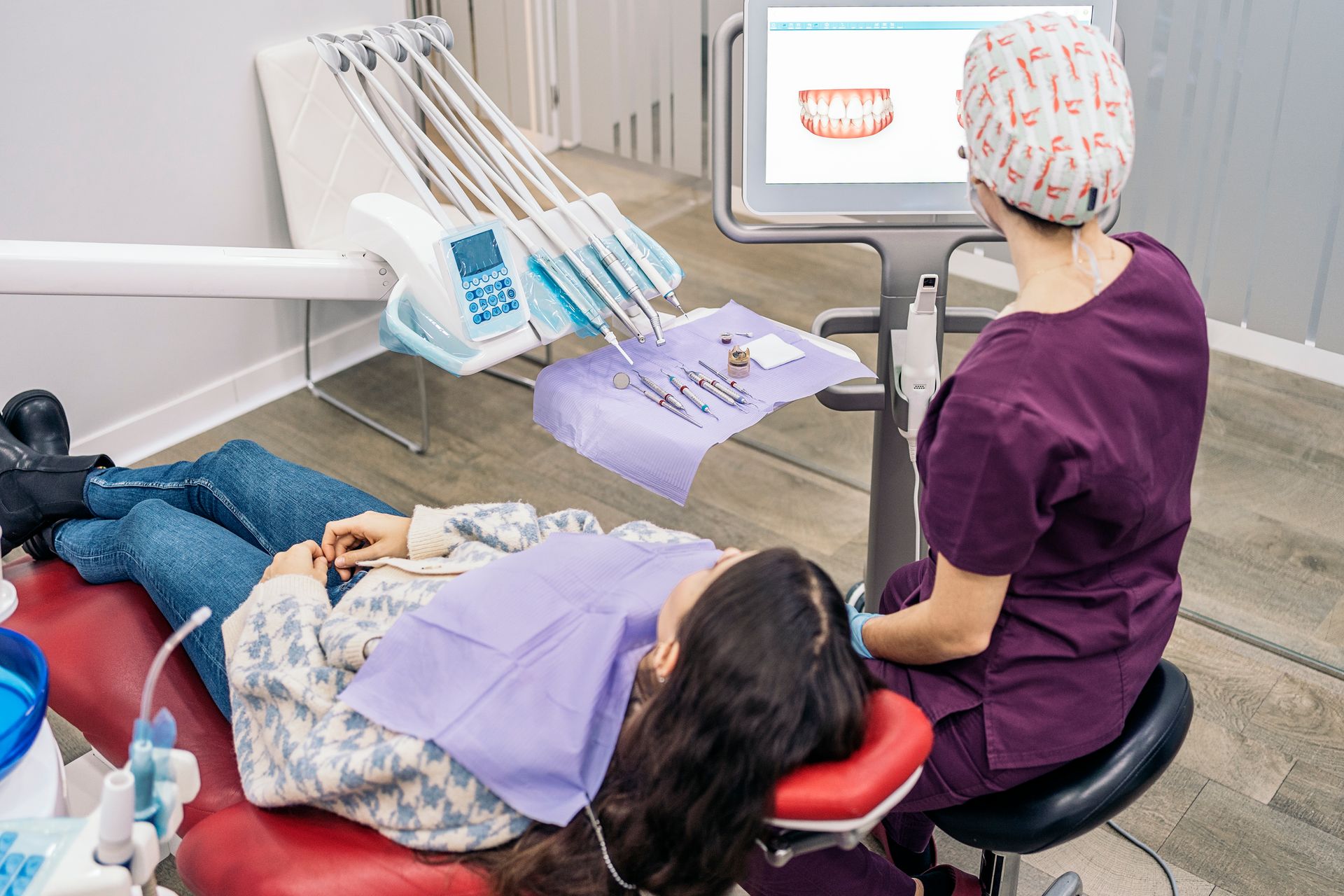 A woman is laying in a dental chair while a dentist looks at her teeth on a computer screen.