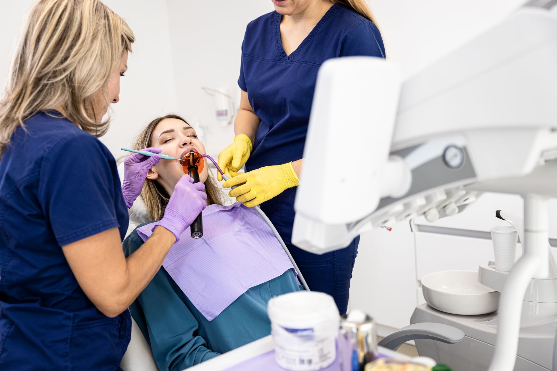 A woman is getting her teeth examined by two female dentists in a dental office.