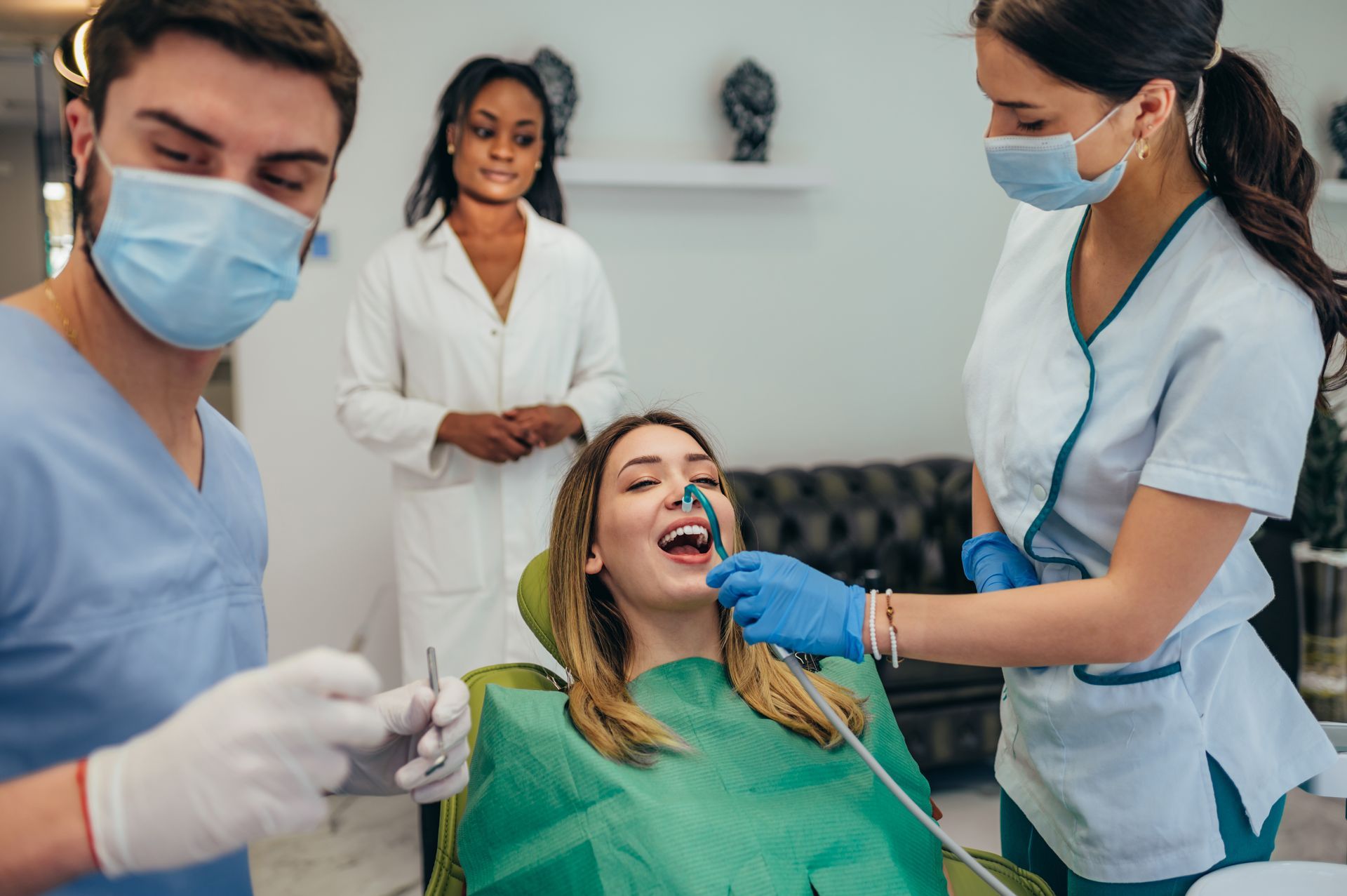 A woman is sitting in a dental chair getting her teeth examined by two dentists.