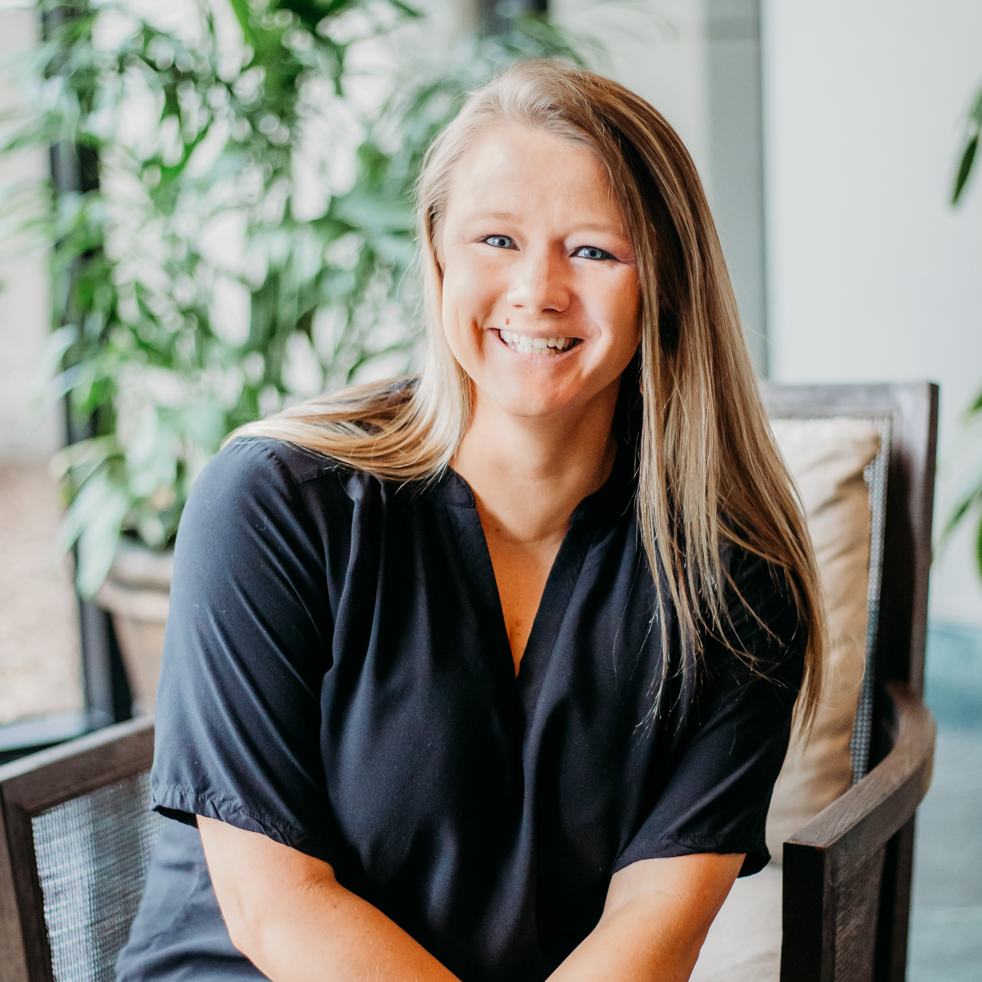 A woman in a black shirt is sitting in a chair and smiling.