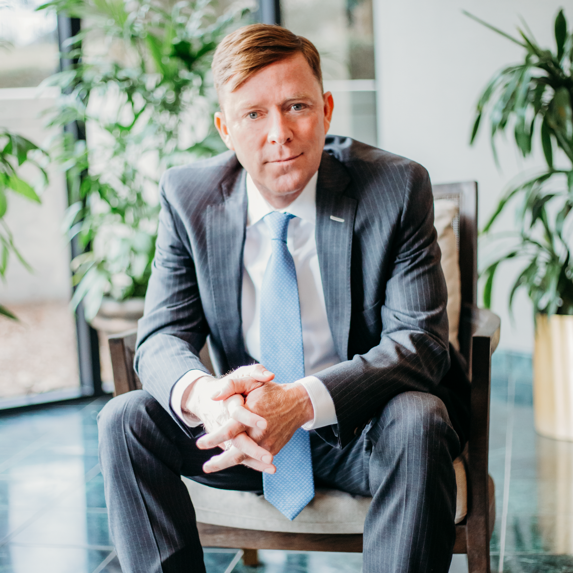 Male personal injury lawyer in a suit and tie is sitting in a chair with his hands folded