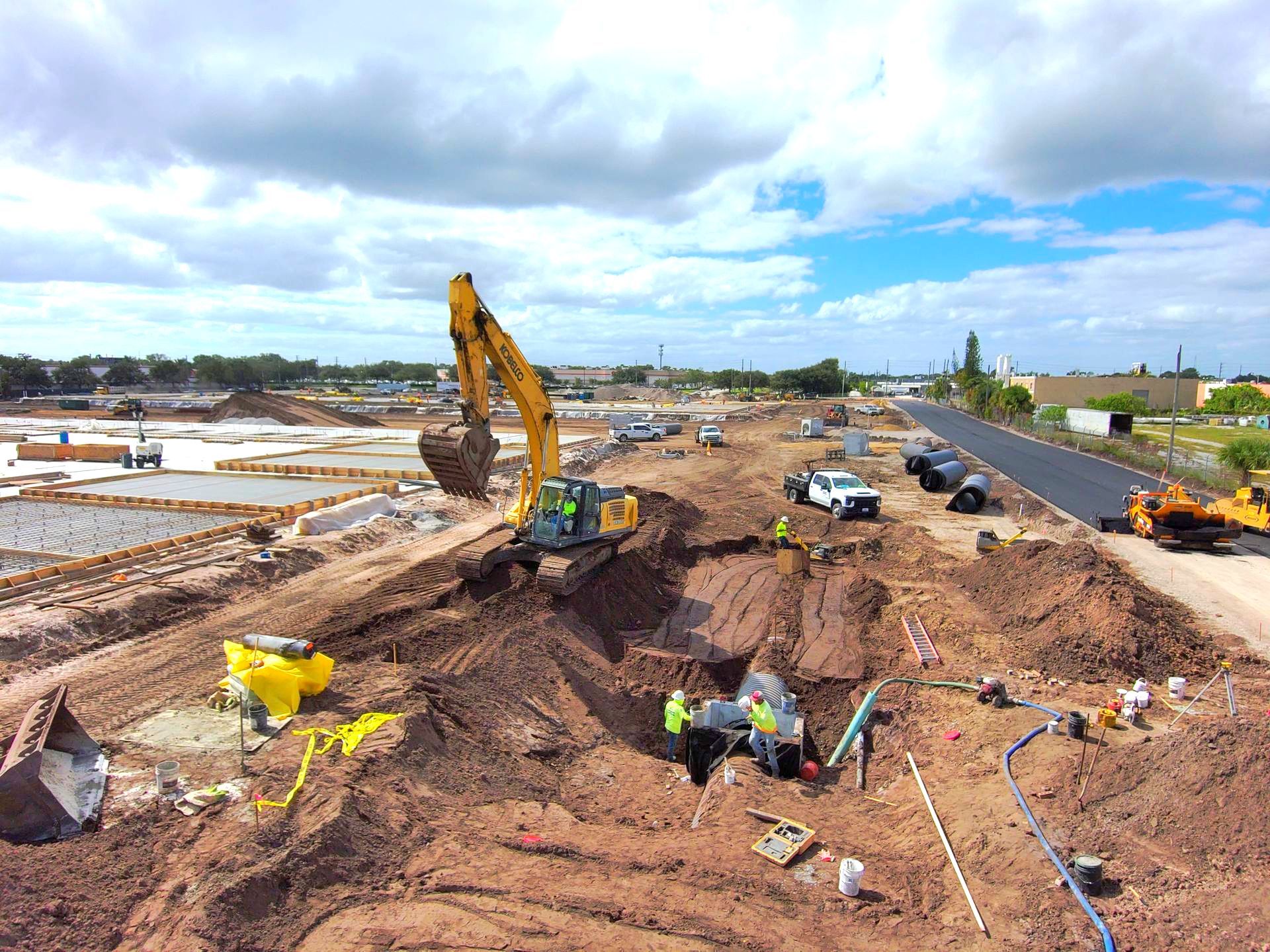 An aerial view of a construction site with a yellow excavator digging a hole.