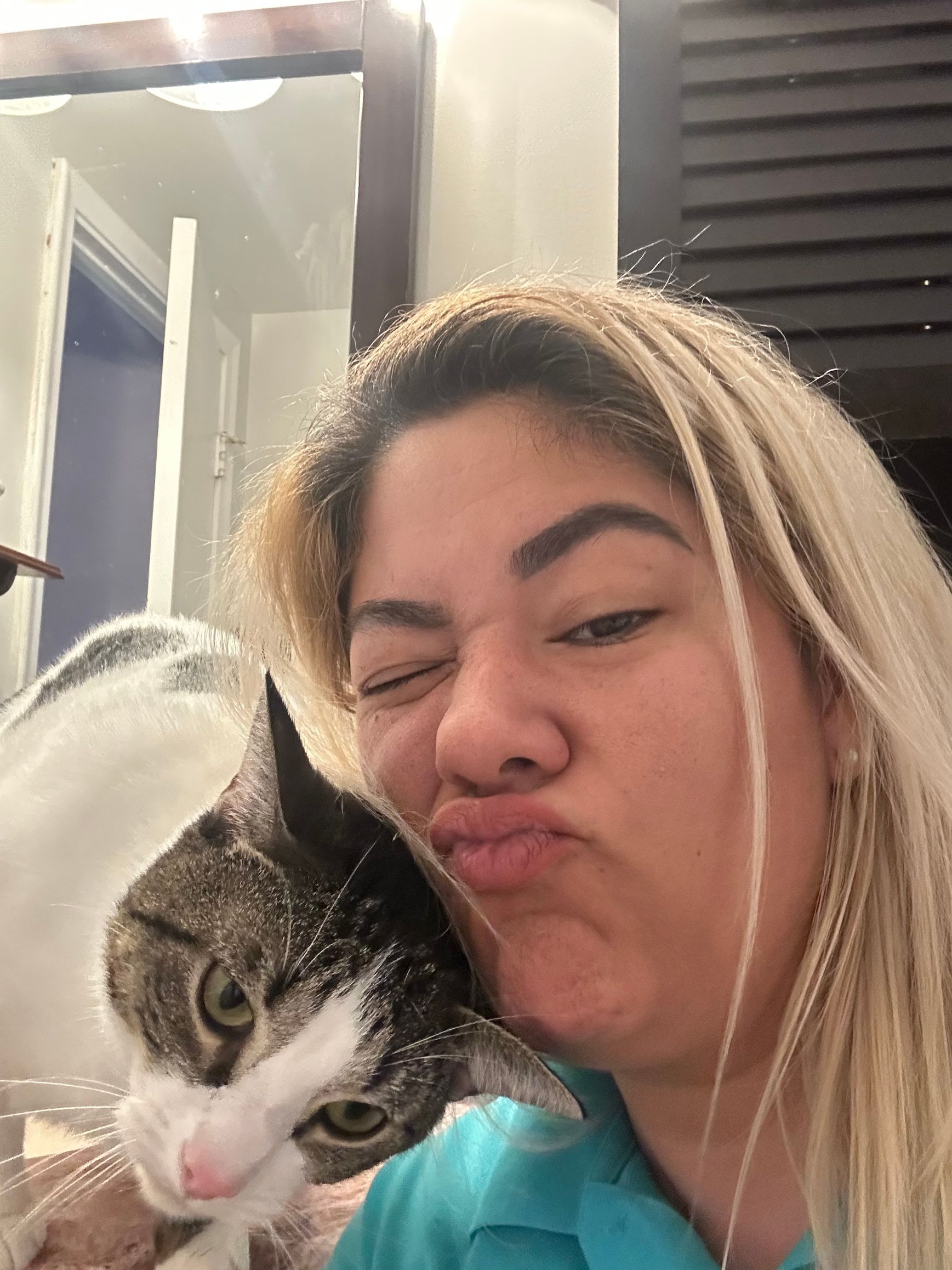 A woman is kissing a cat on the nose.