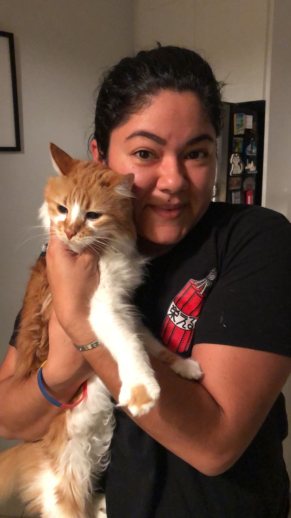 A woman in a black shirt is holding an orange and white cat