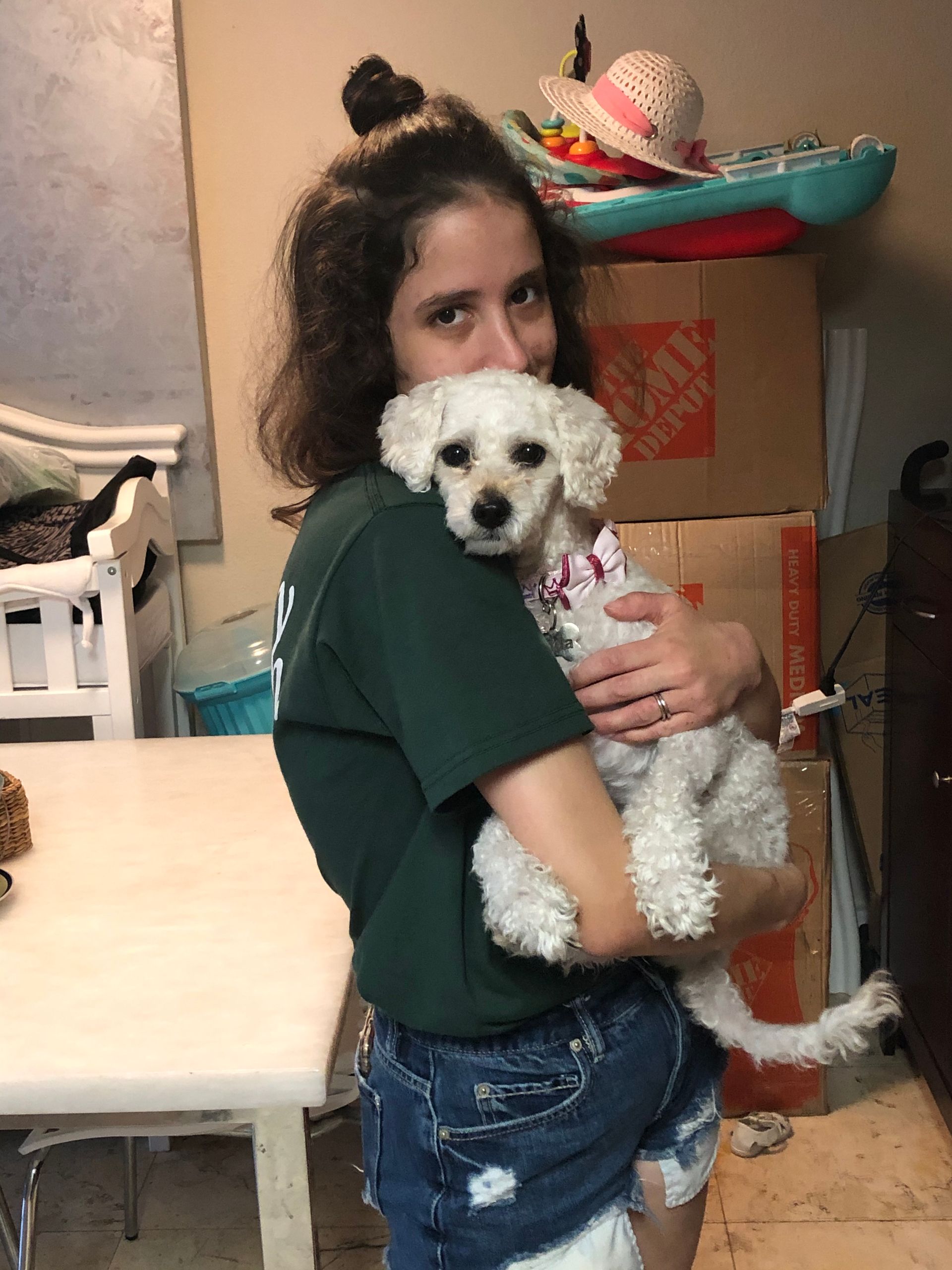 A woman in a green shirt is holding a small white dog
