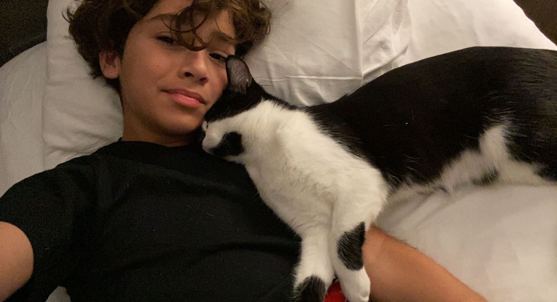 A young boy is laying on a bed with a black and white cat.