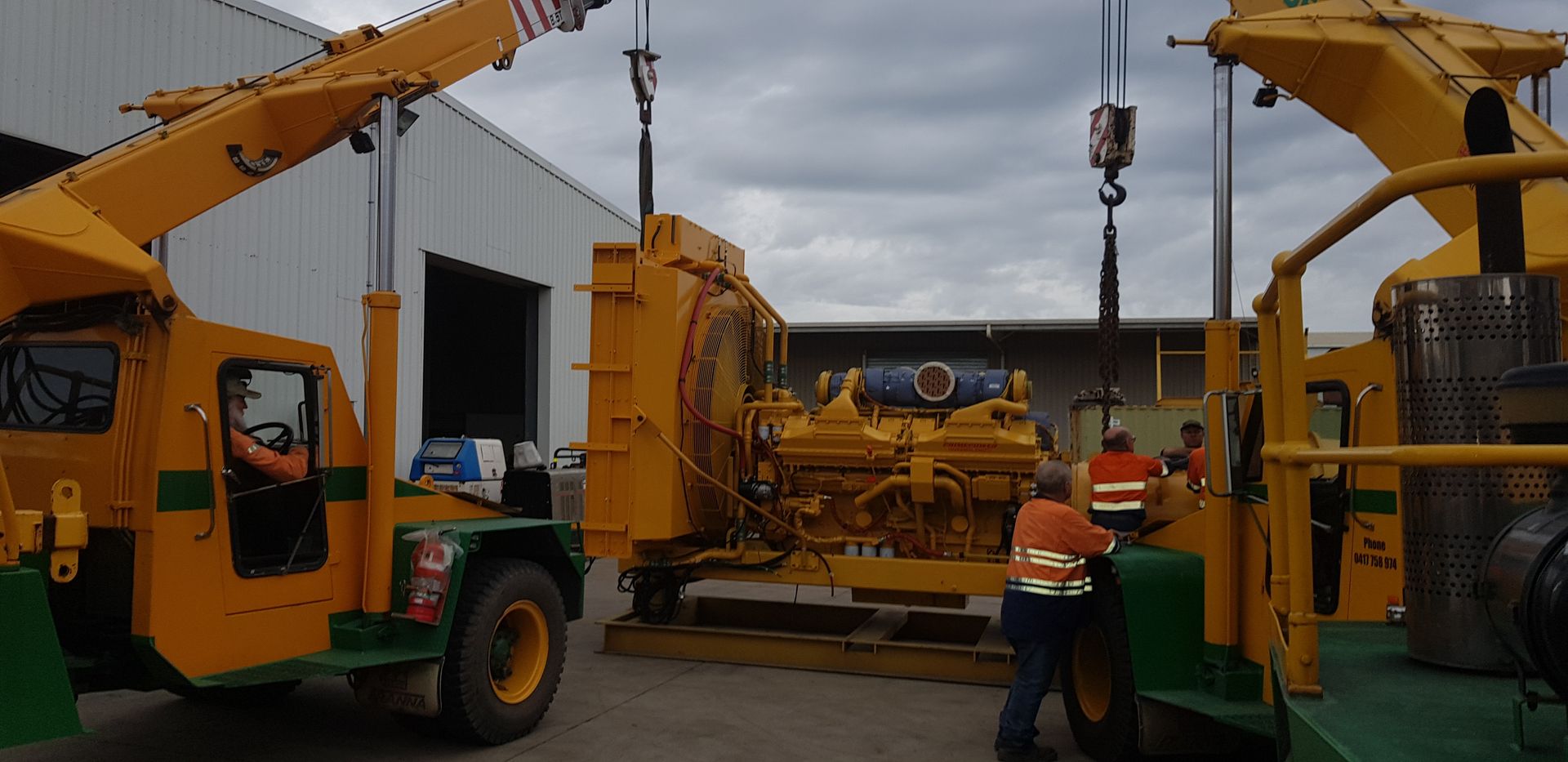 Two yellow cranes lift a large yellow machine outdoors near a building. Workers in orange vests supervise— Statewide Lift & Shift Pty Ltd In Paget, QLD