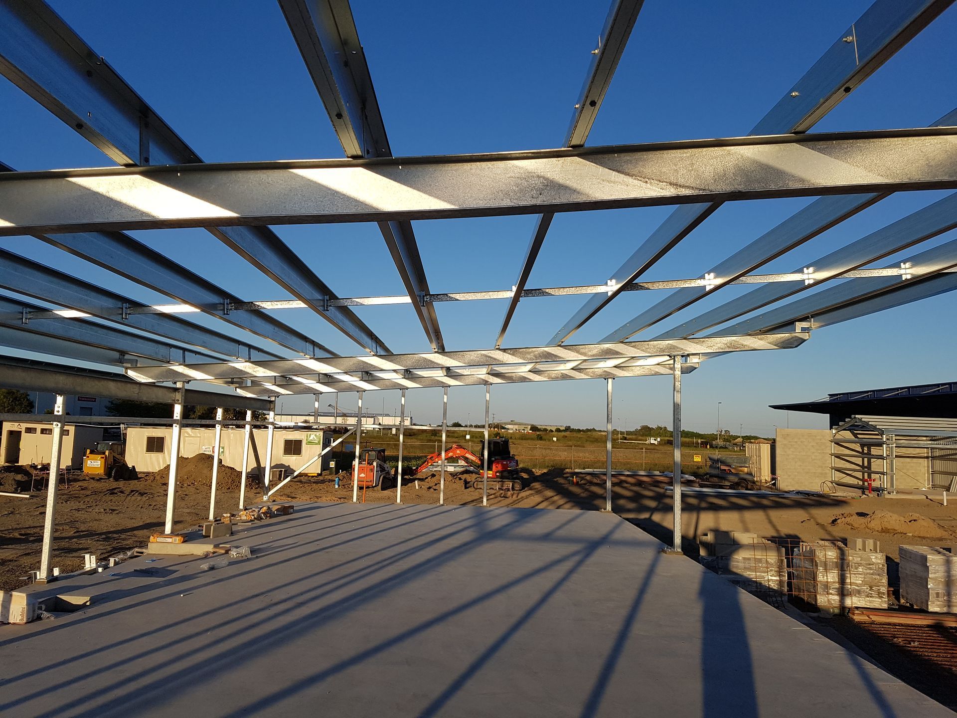 Steel framework of a building under construction, viewed from concrete slab, with clear blue sky — Statewide Lift & Shift Pty Ltd In Sarina, QLD